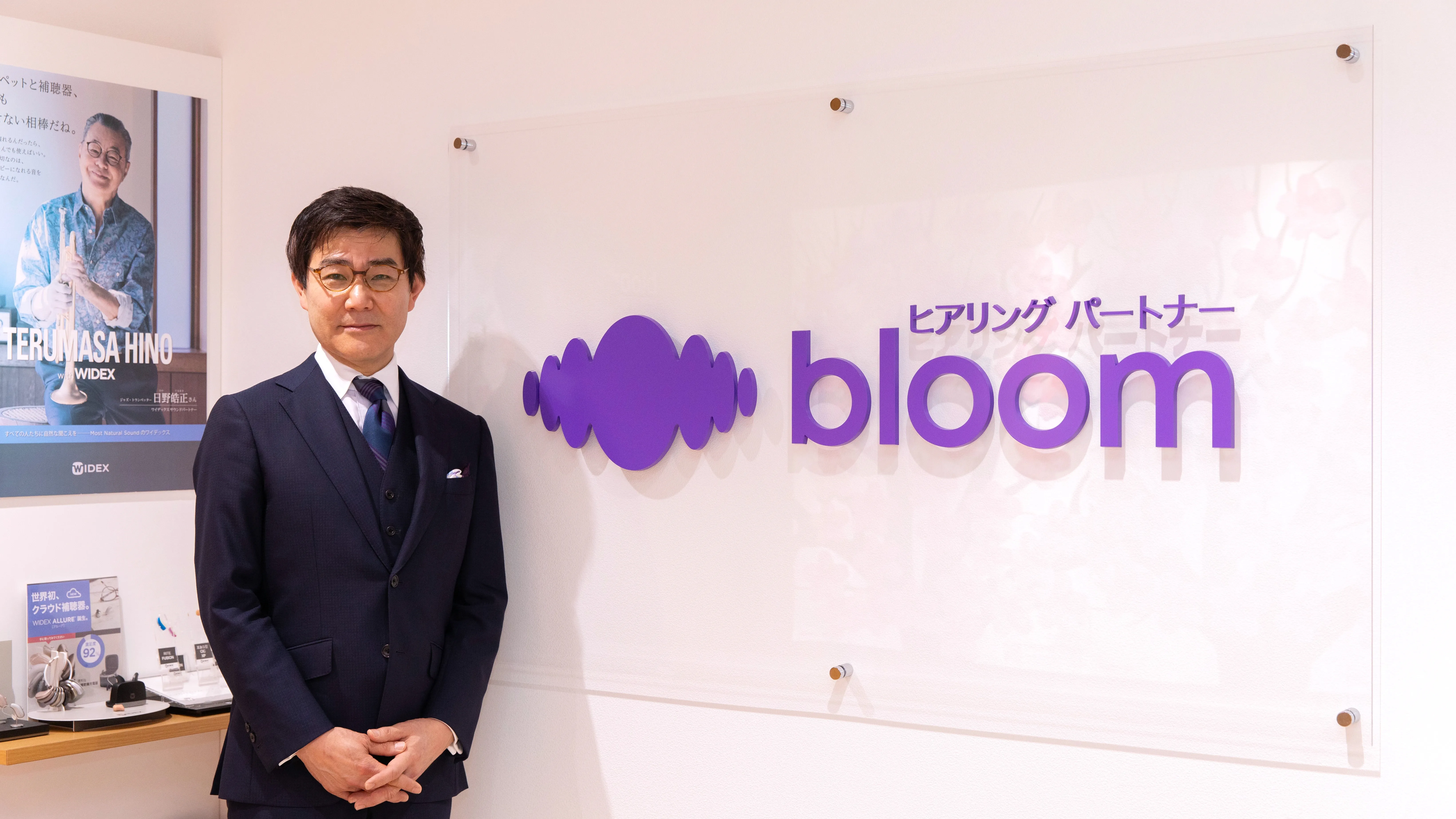 ブルーム代表取締役社長の松崎がブルームのロゴパネル隣に立つ写真