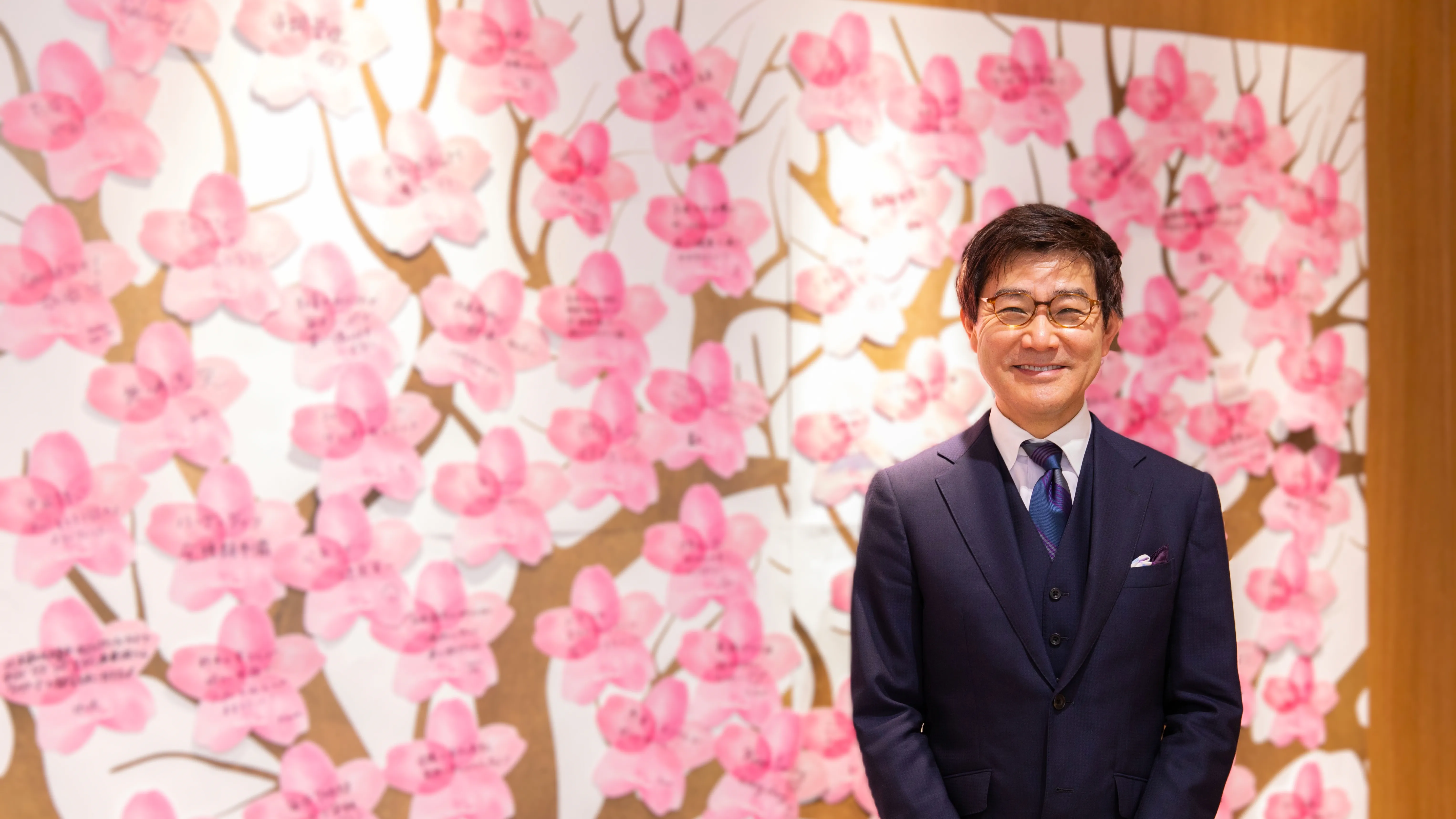 ブルーム代表取締役社長の松崎が、社員の夢を表した桜パネルの前に立つ写真