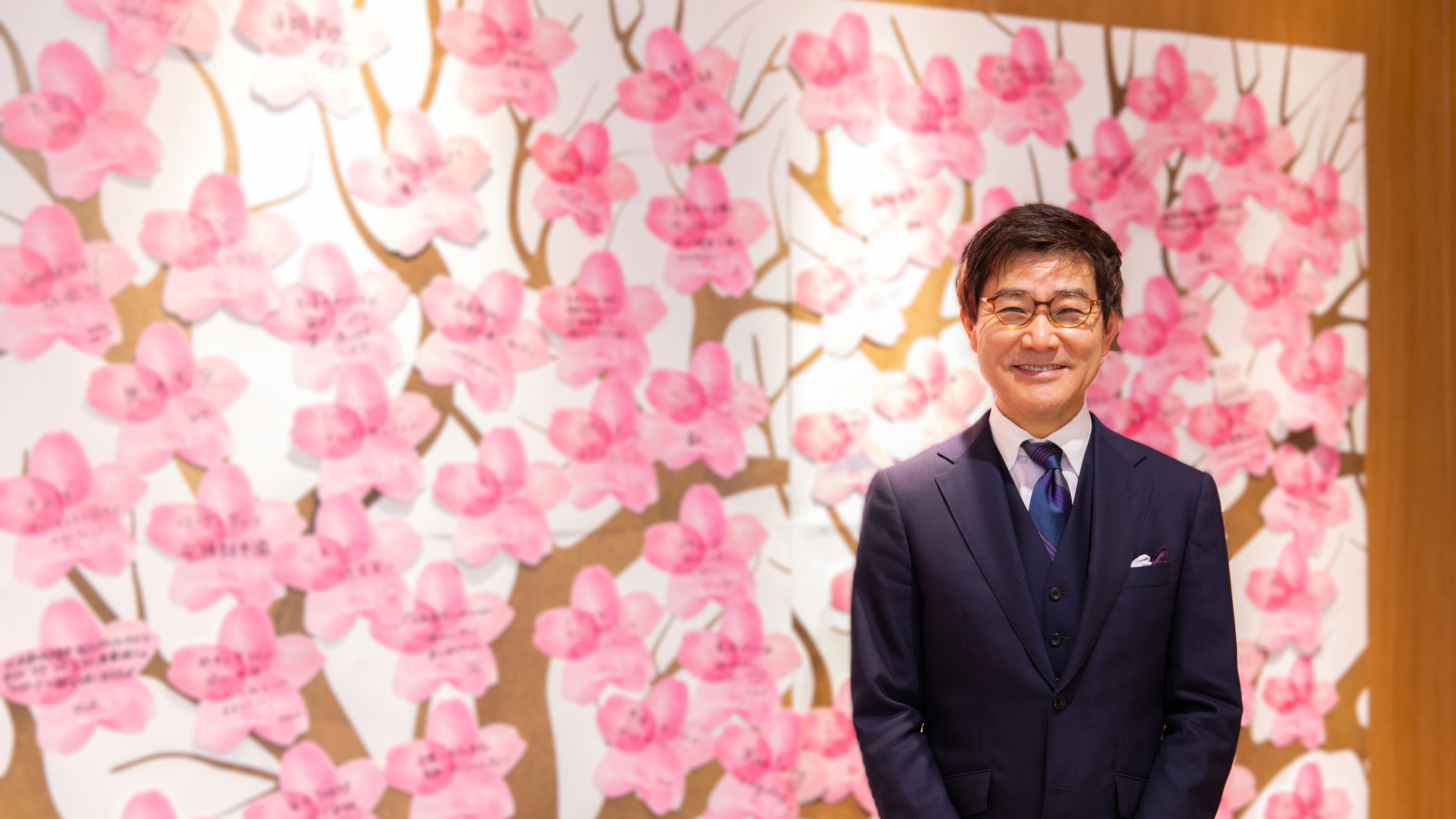 ブルーム代表取締役社長の松崎が、社員の夢を表した桜パネルの前に立つ写真