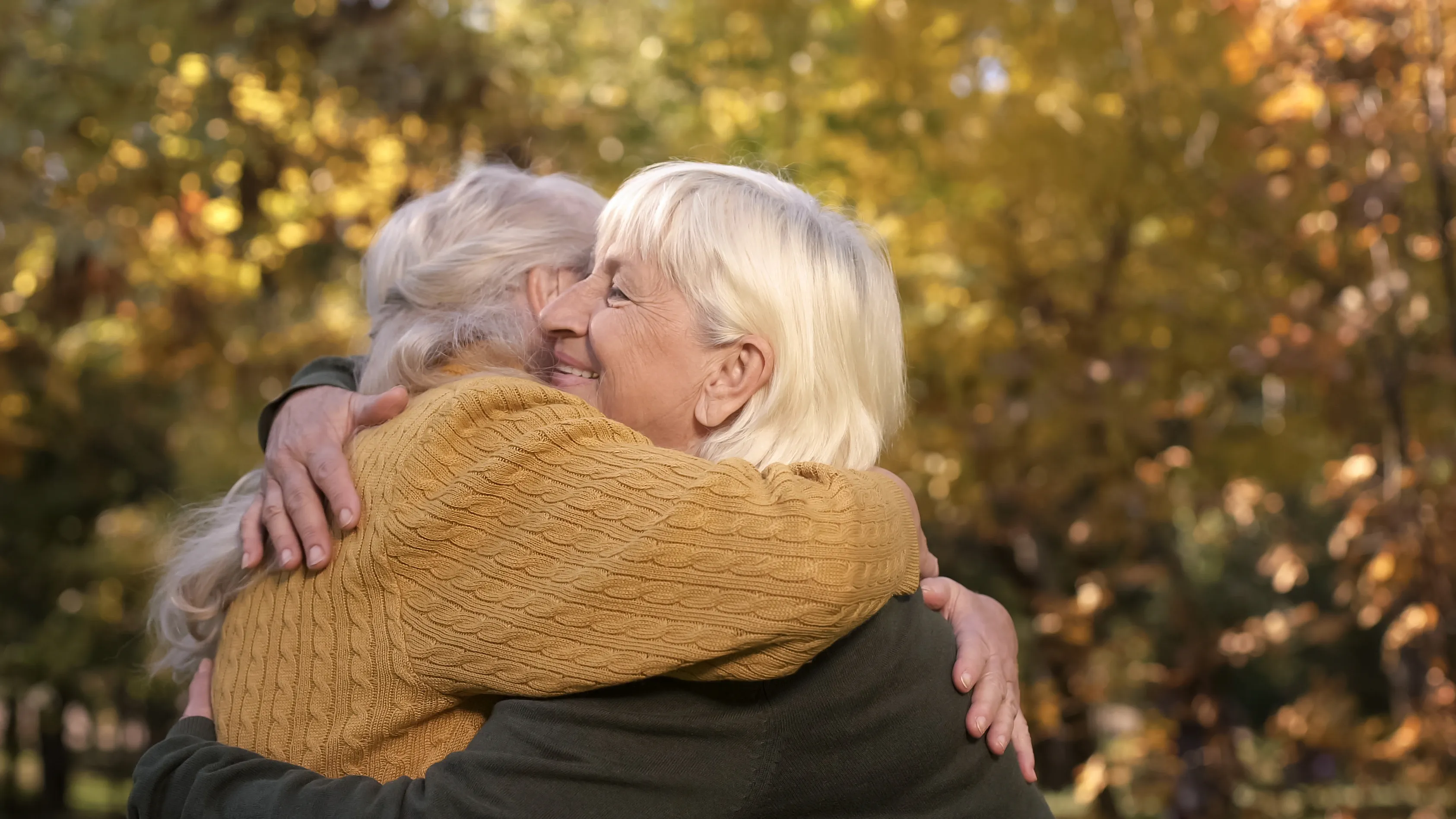 Elderly friends outside, finding it hard to hear each other due to hearing loss.