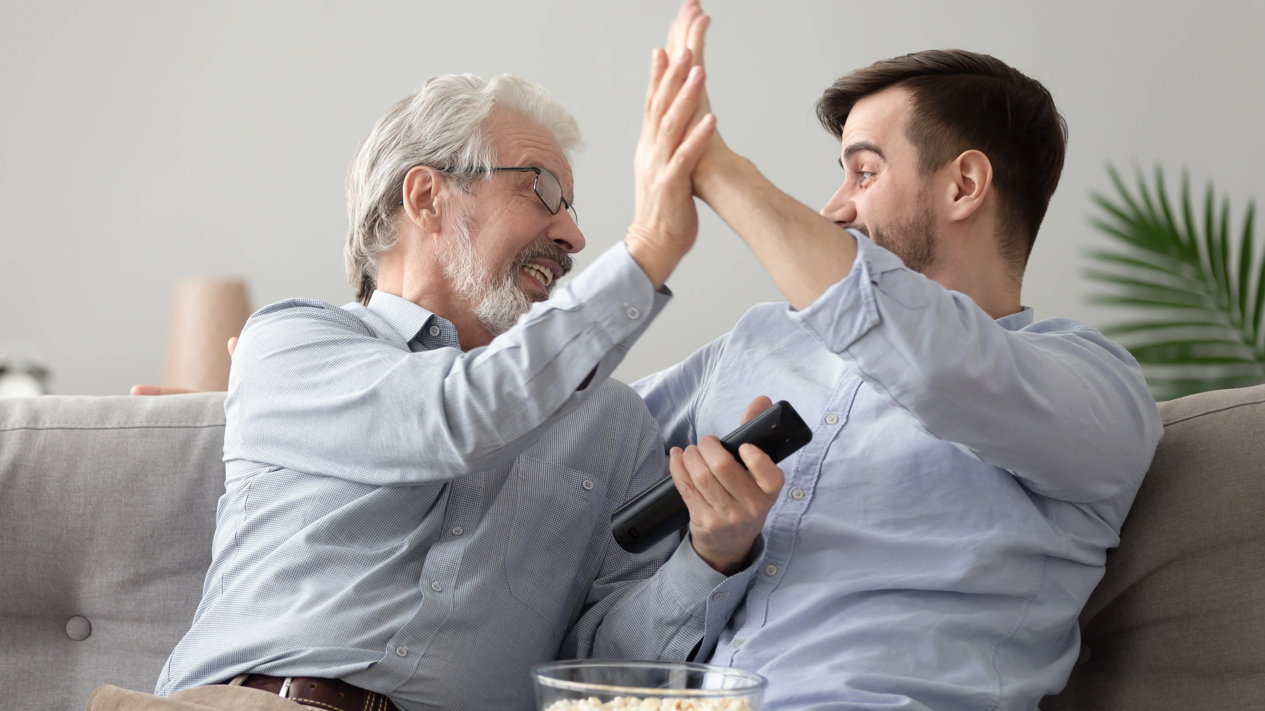 Father and son watching TV, struggling to hear the dialogue clearly due to hearing loss.