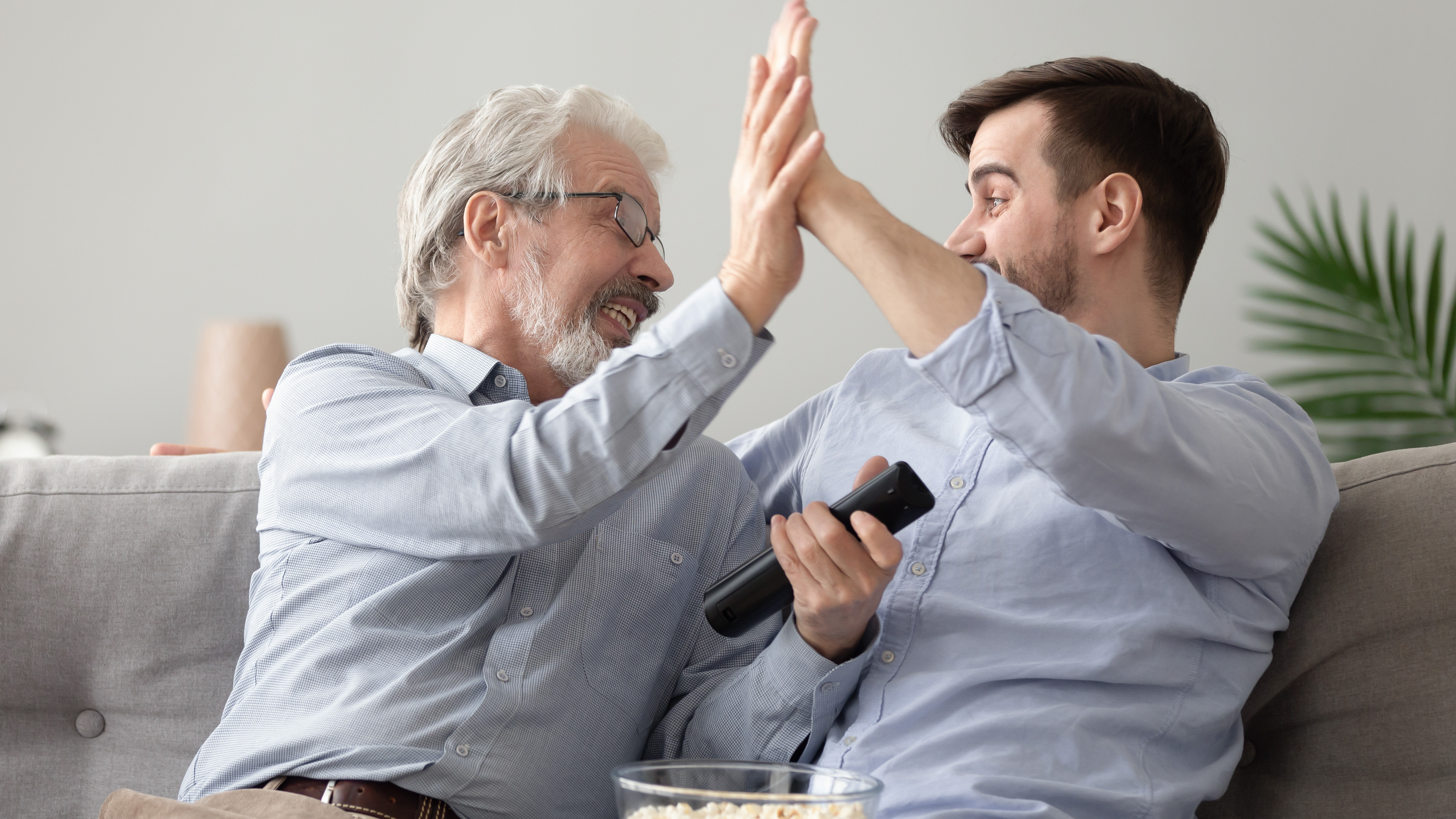 Father and son watching TV, struggling to hear the dialogue clearly due to hearing loss.