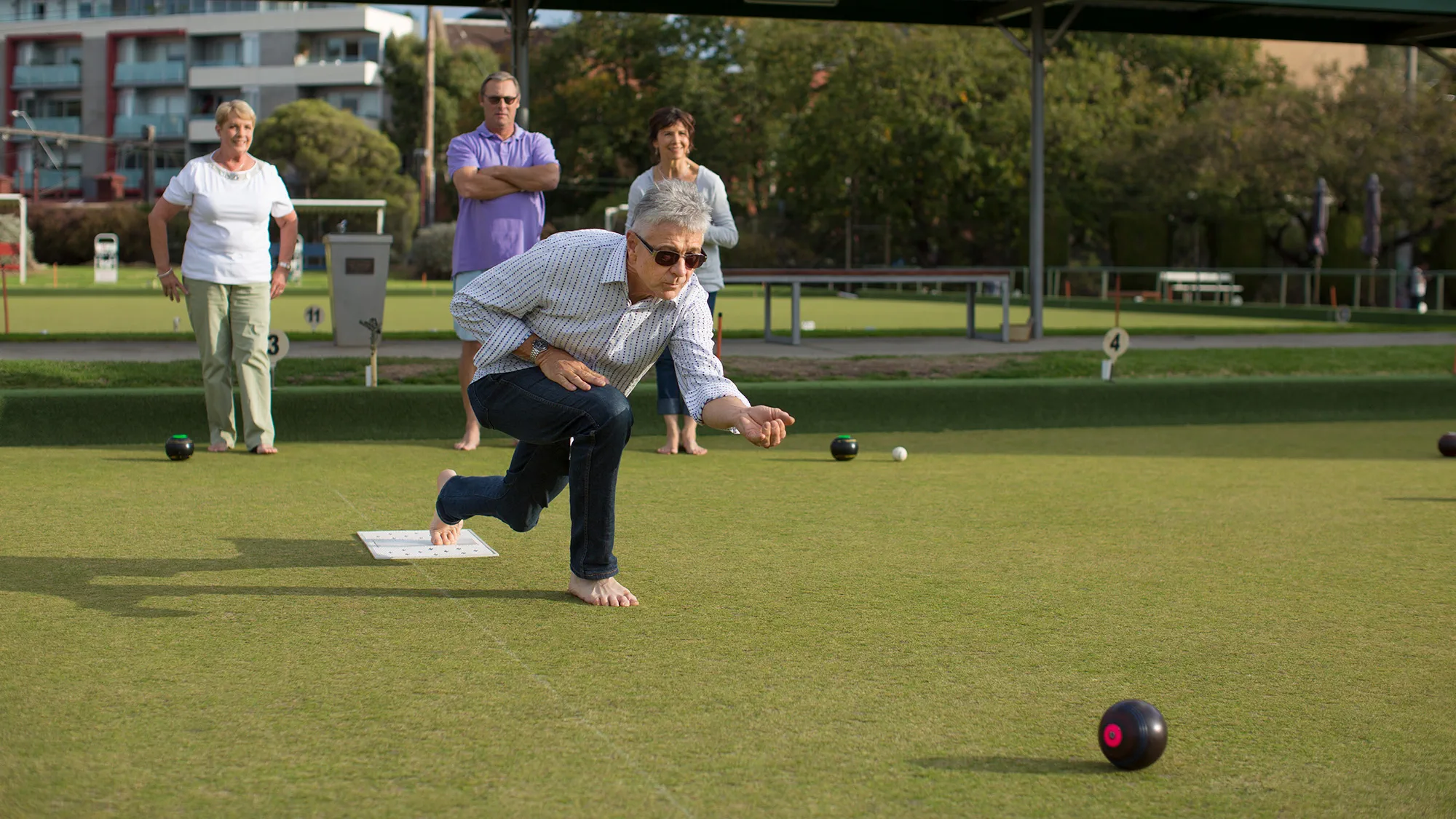 A group of friends playing lawn bowls together, with one of them wearing hearing aids, enjoying social interaction despite hearing challenges.