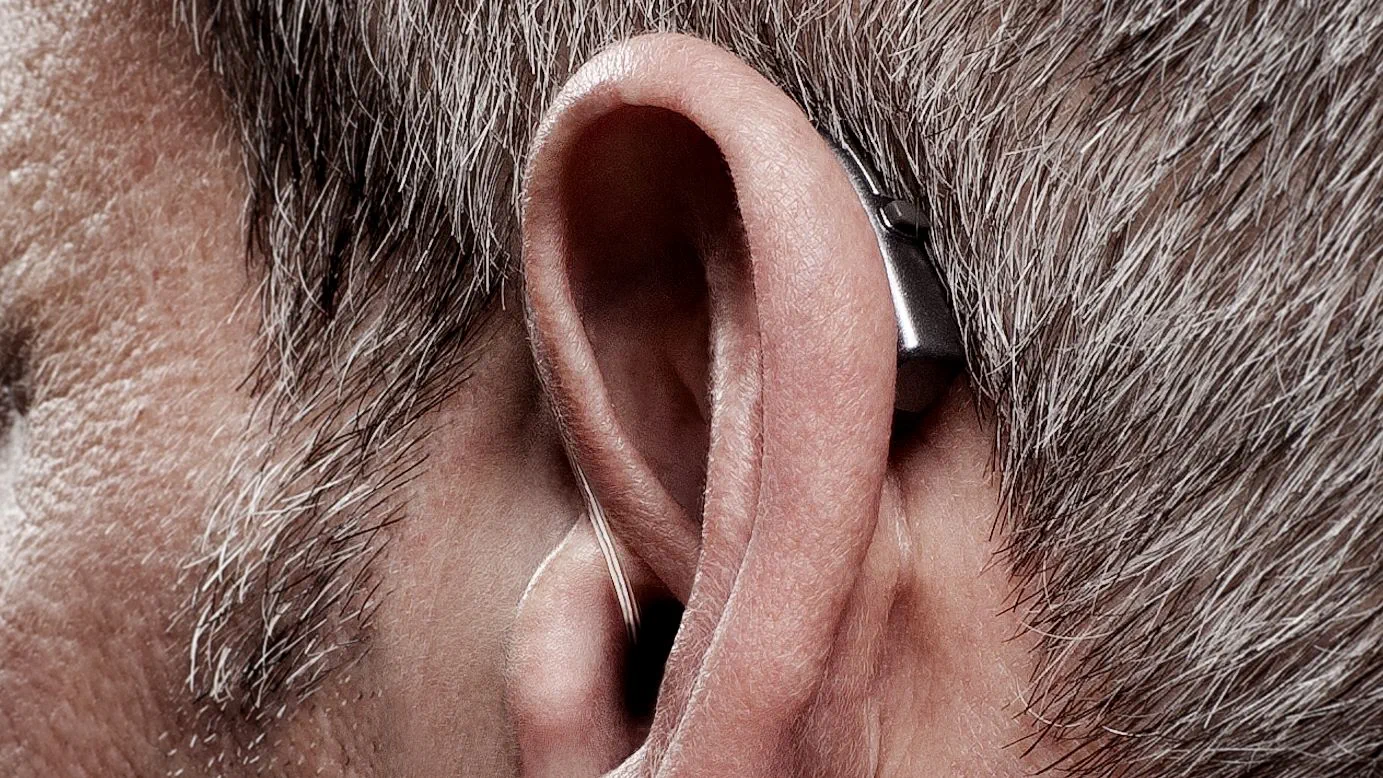 Man with behind-the-ear hearing aids, still struggling to hear clearly