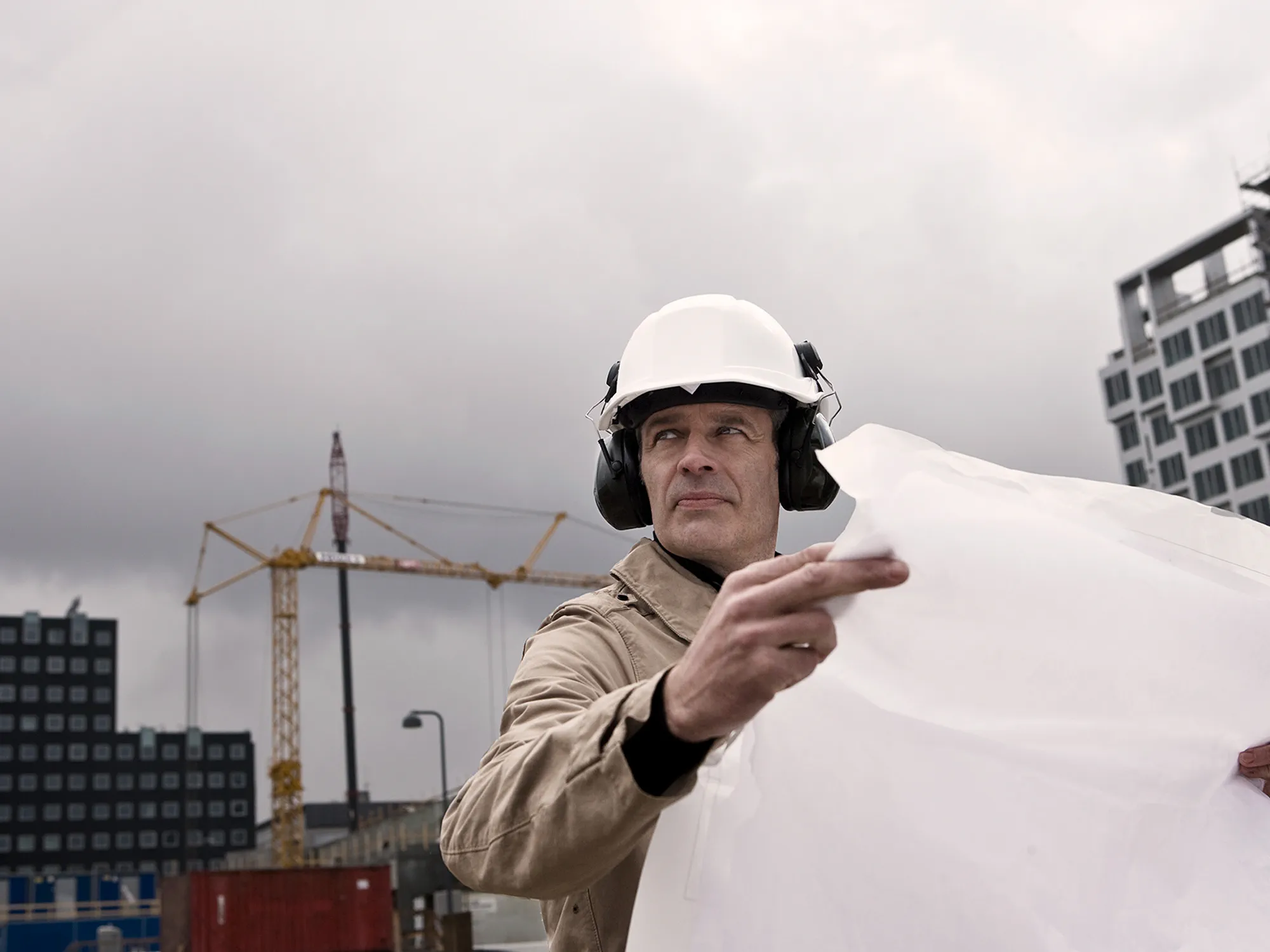 A man at a construction site, wearing hearing protection, experiencing hearing loss, highlighting occupational risks to hearing health.