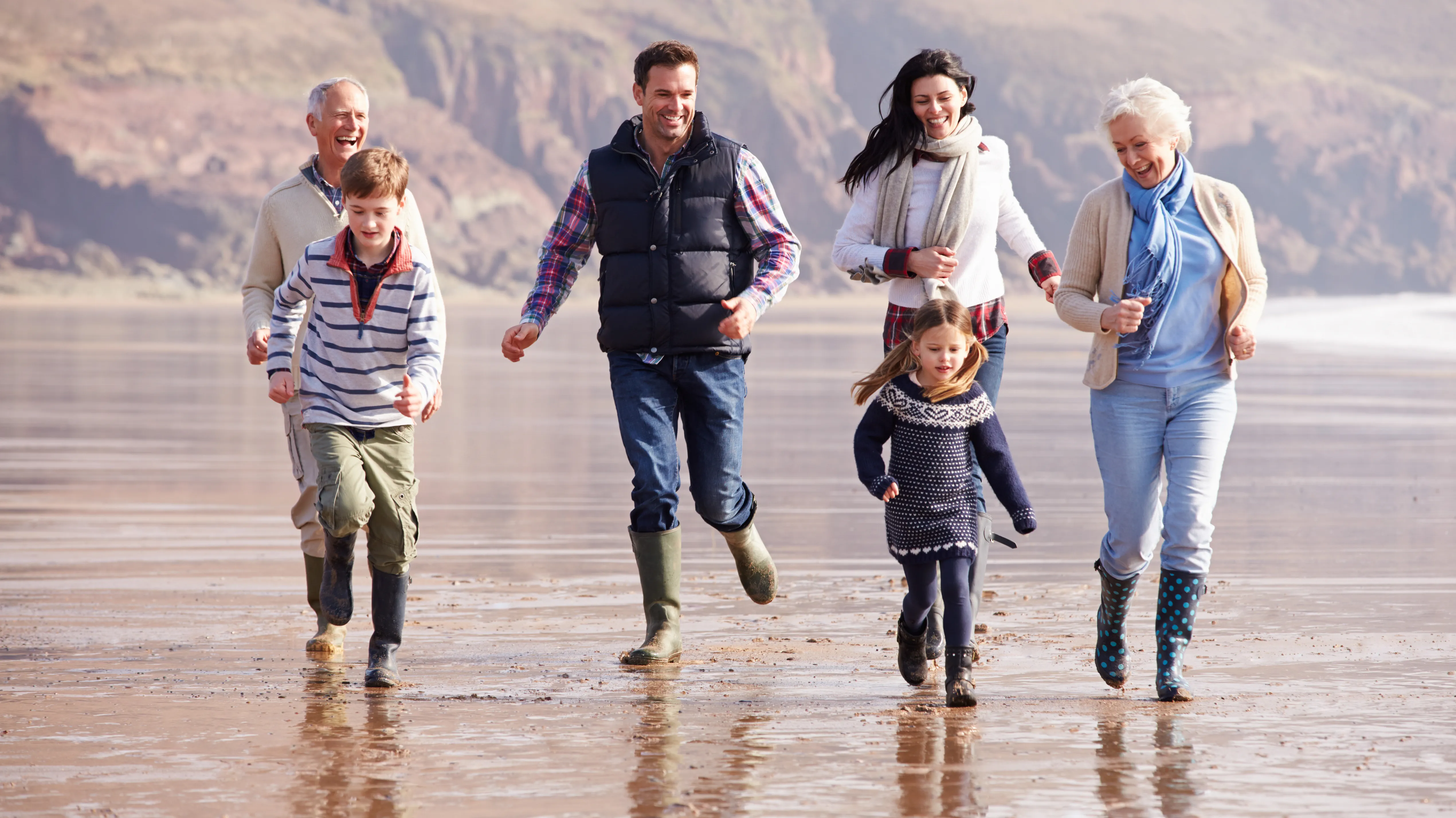 Multi generation family running on winter beach using hearing aids