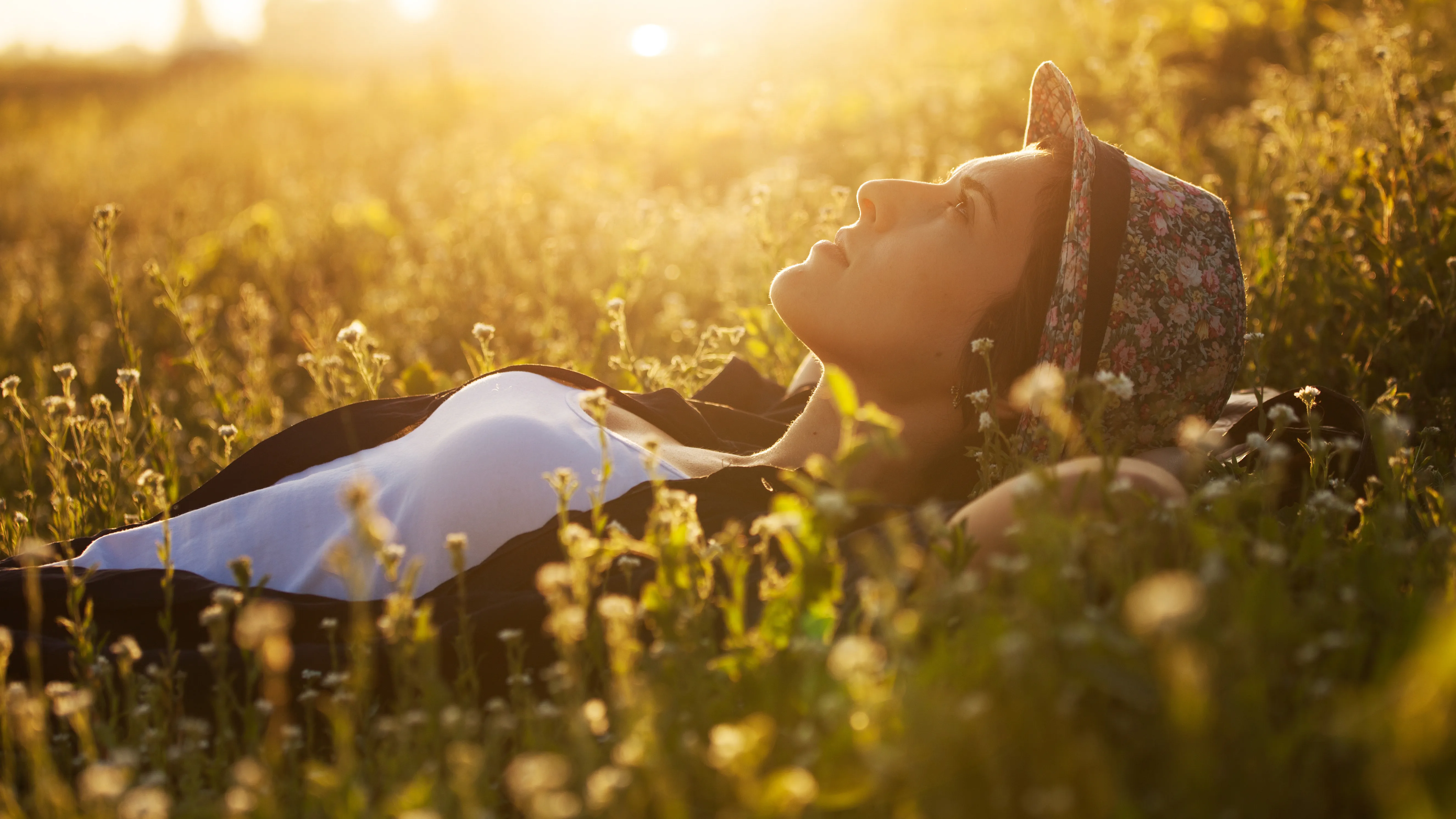 Happy girl lies among the wild flowers on a summer evening using hearing aids