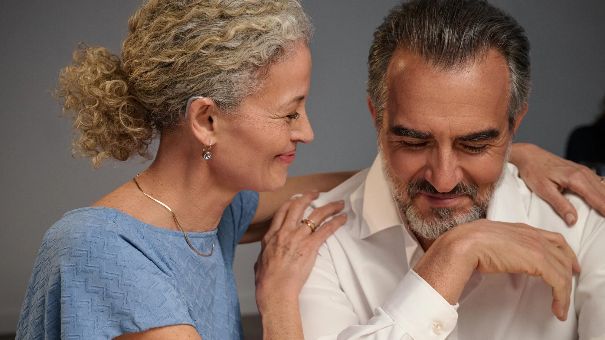 Couple smiling proudly, shown up close with their hearing aids visible.