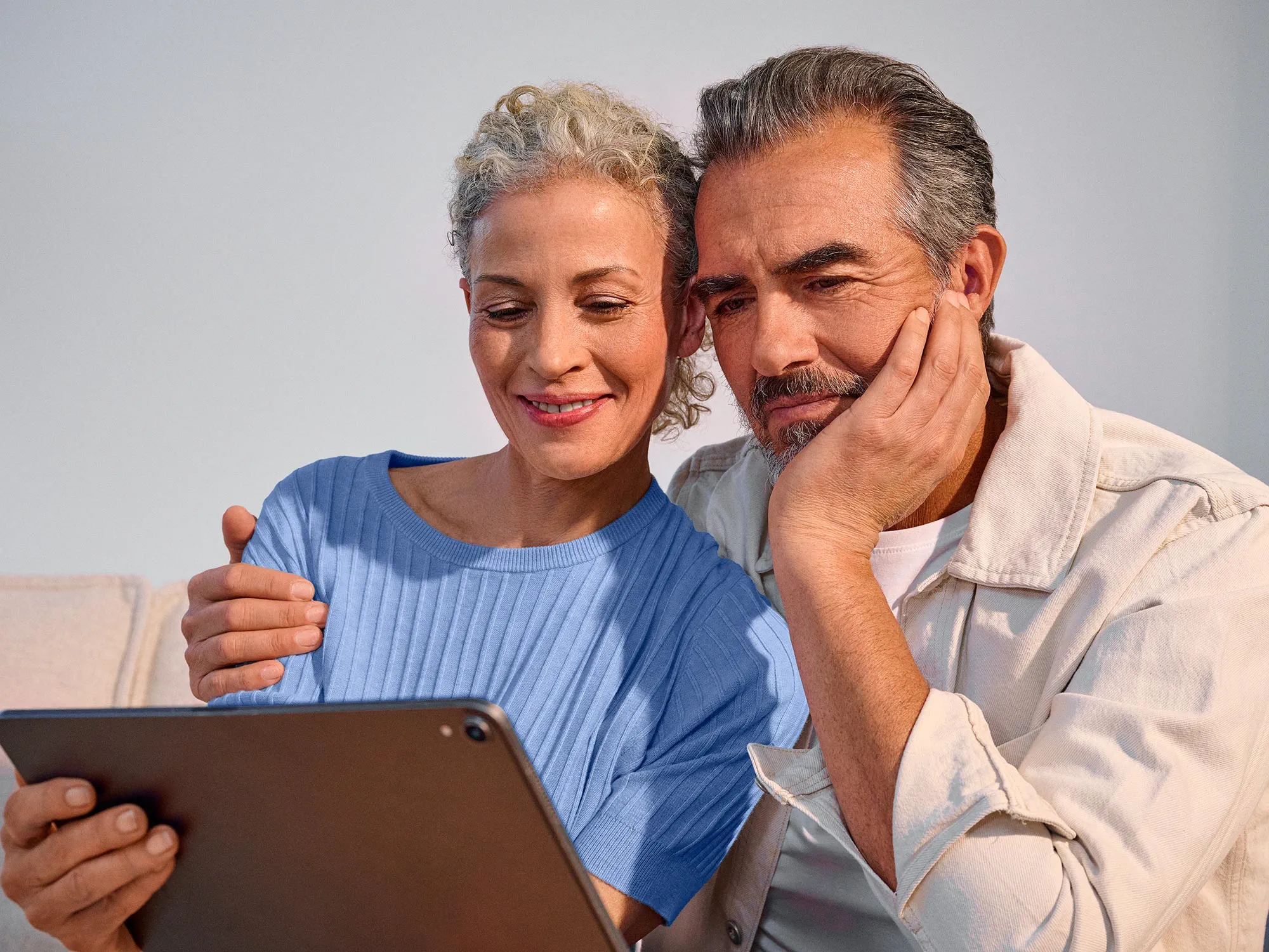 Couple using technology closely together, both wearing hearing aids.