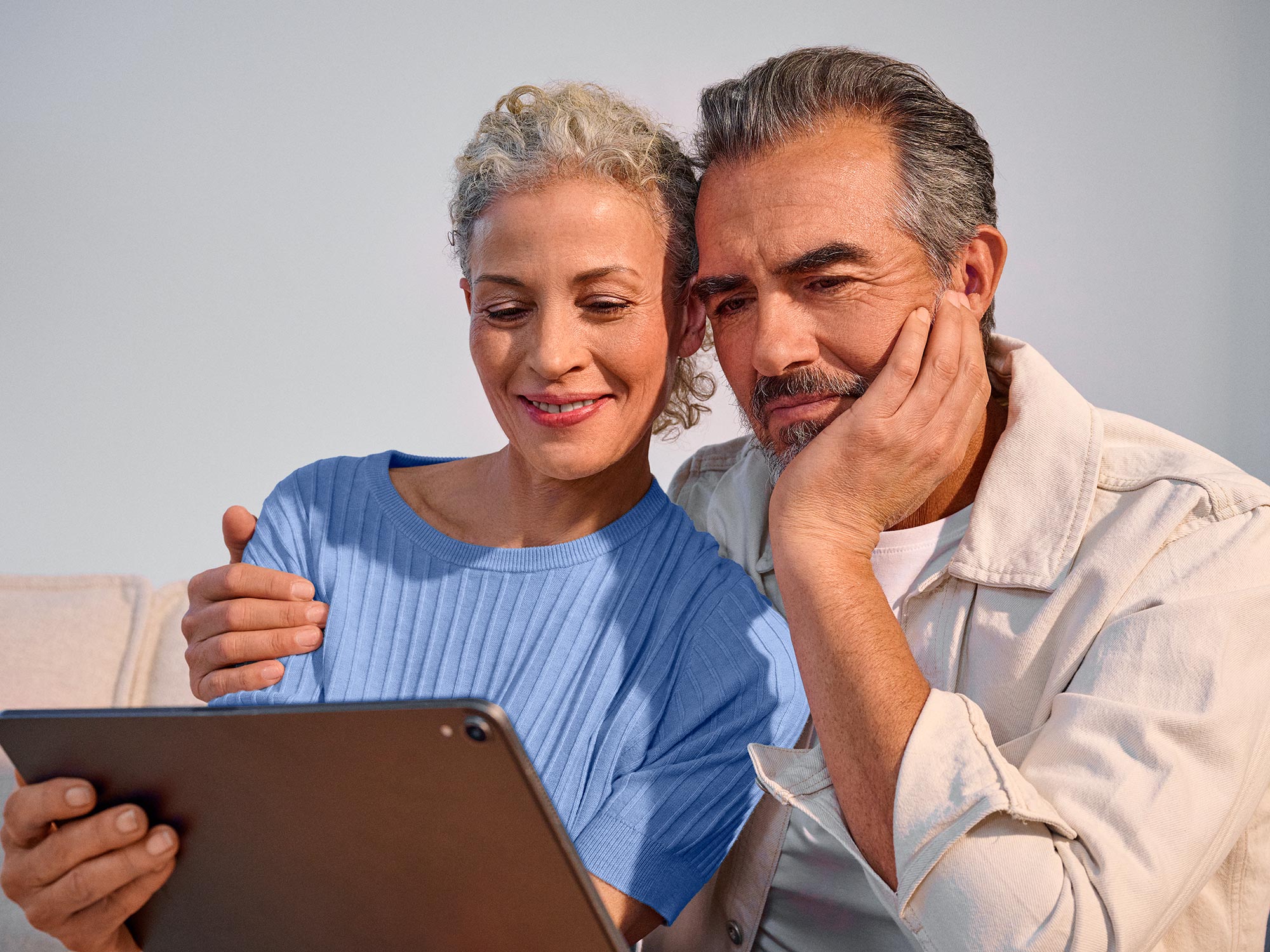 Couple using technology closely together, both wearing hearing aids.