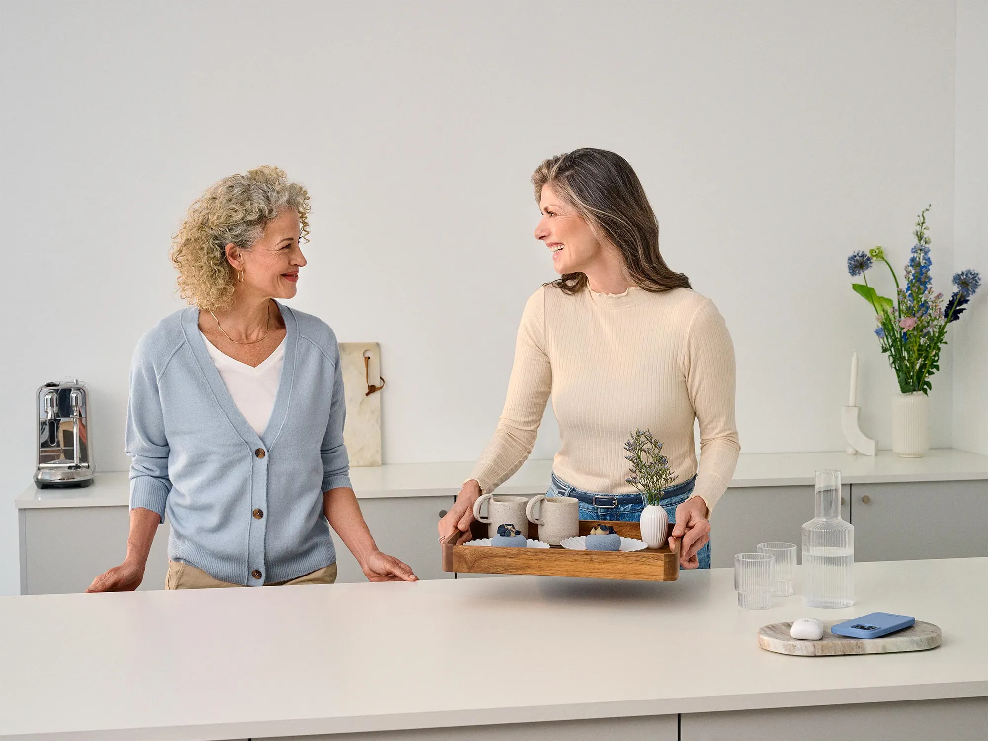 Woman hosting a friend at home, wearing hearing aids.