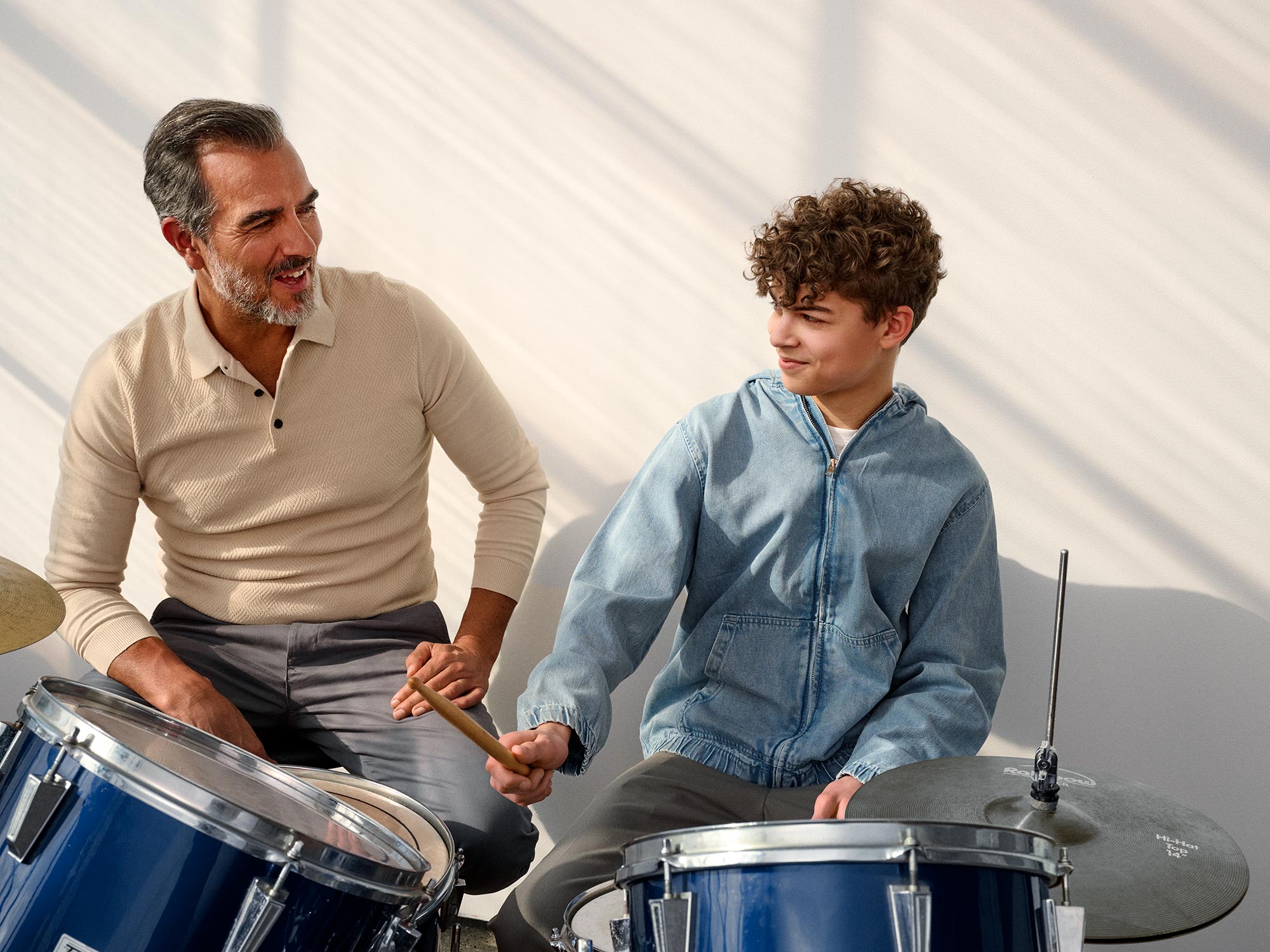 Grandparent and child playing the drums together, both wearing hearing aids.