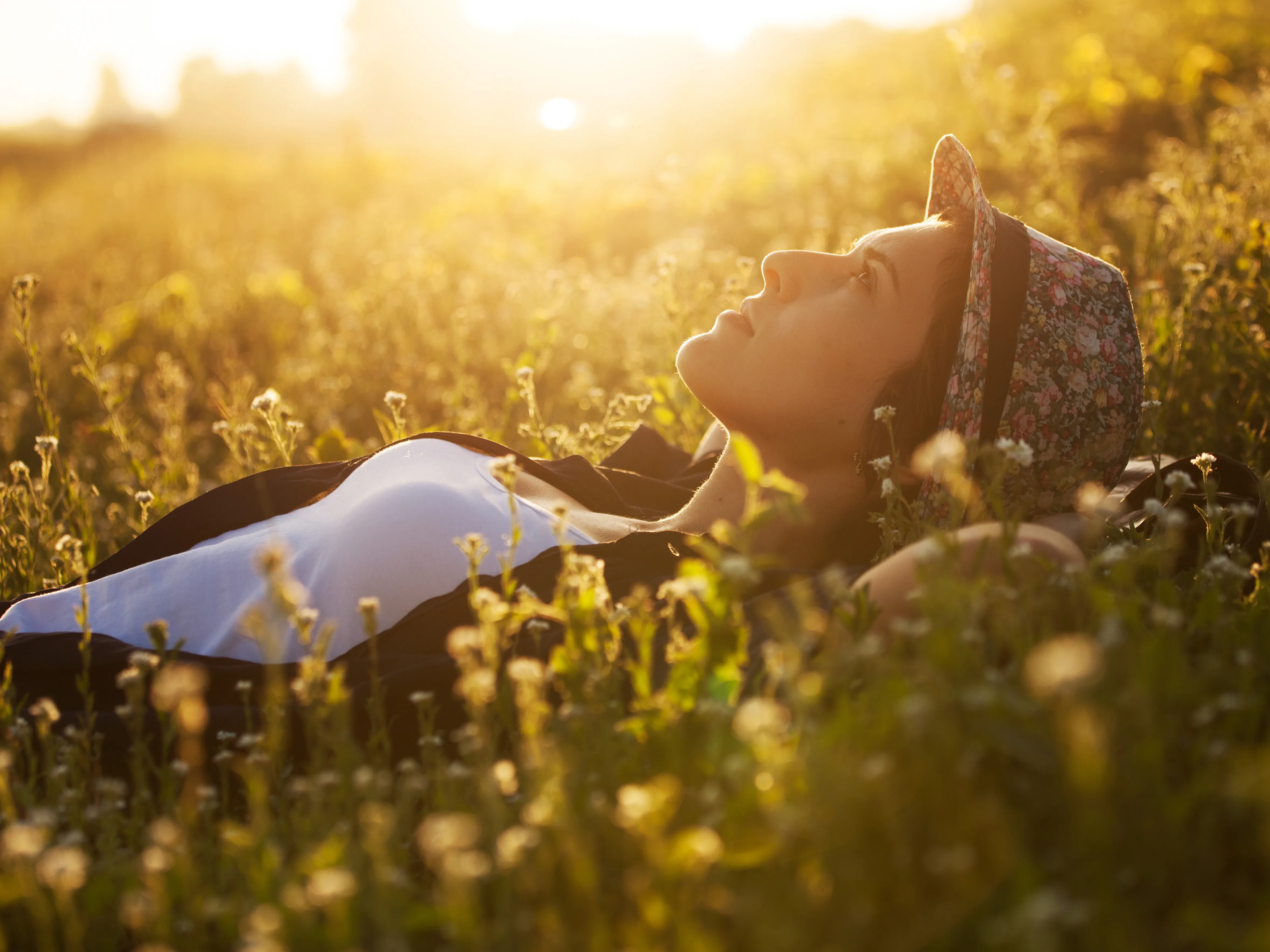 Happy girl lies among the wild flowers on a summer evening using hearing aids
