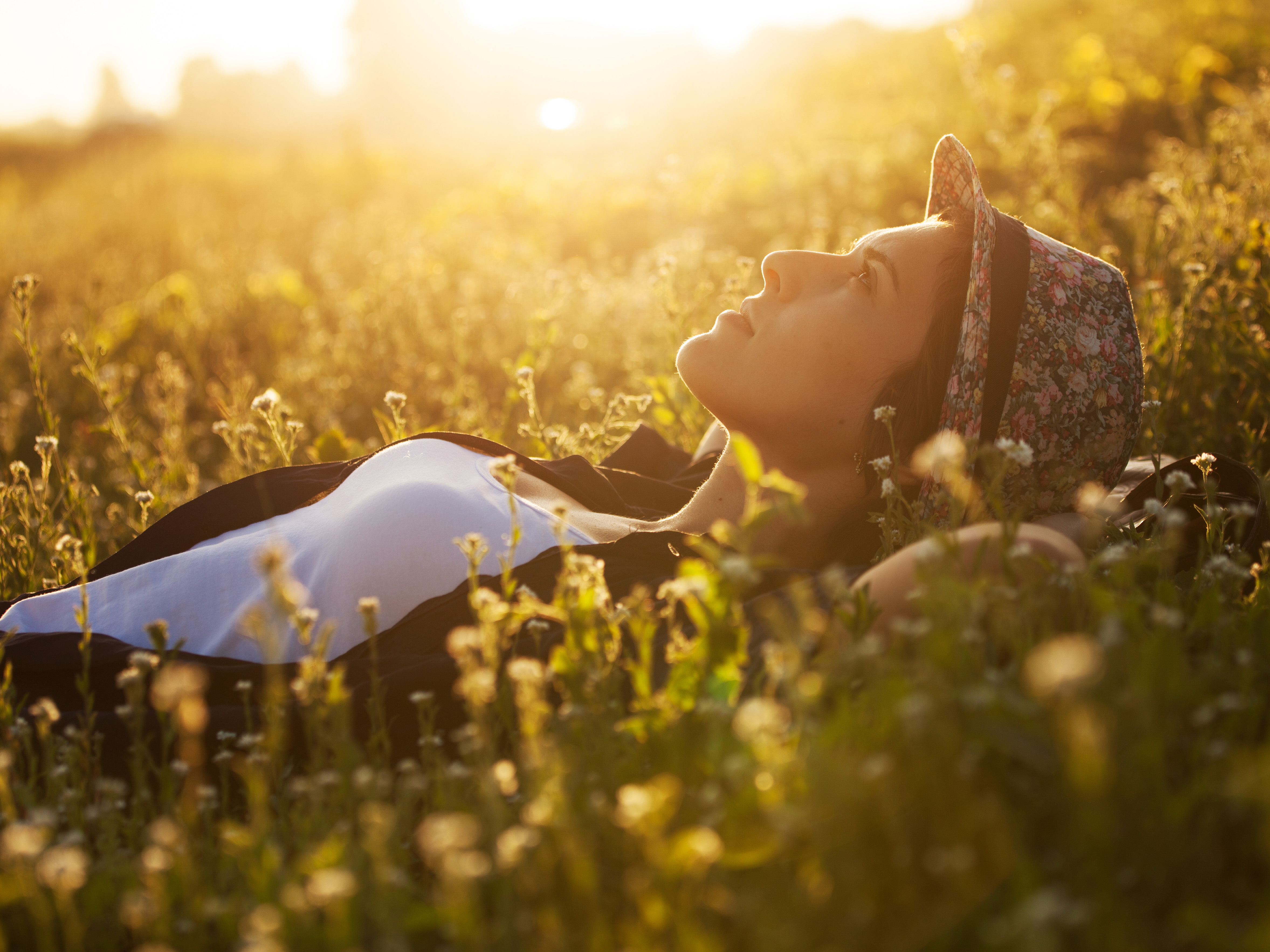 Happy girl lies among the wild flowers on a summer evening using hearing aids