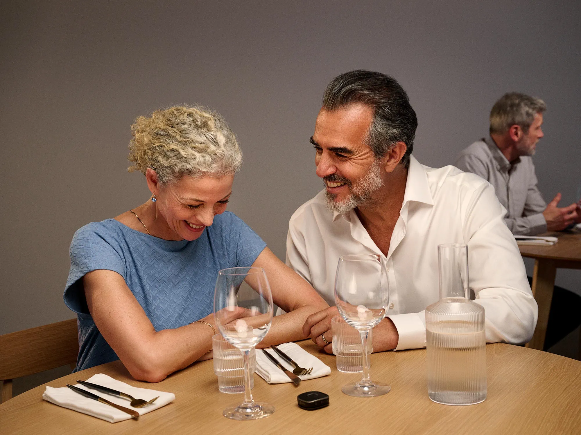 Laughing couple enjoying dinner, celebrating hearing improvement.