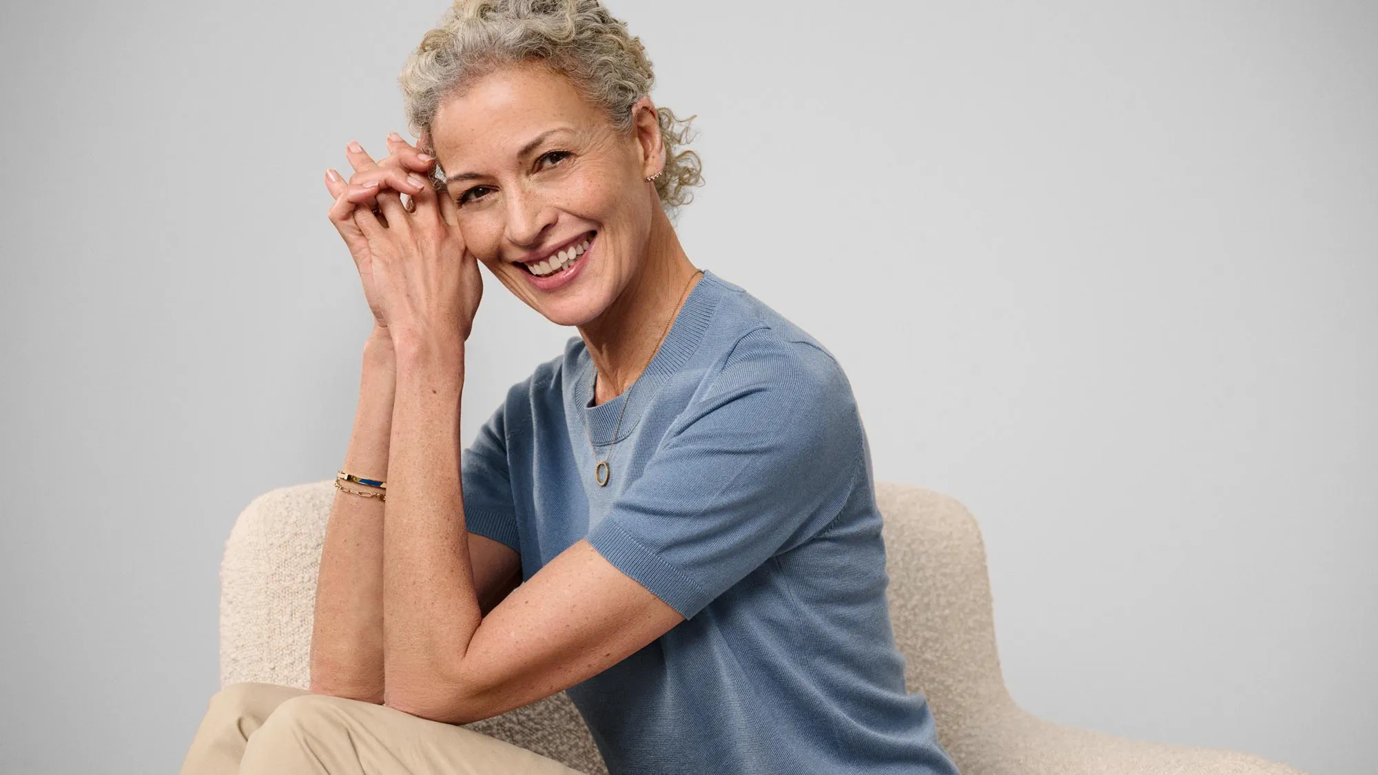 Happy woman sitting, showcasing hearing aids.