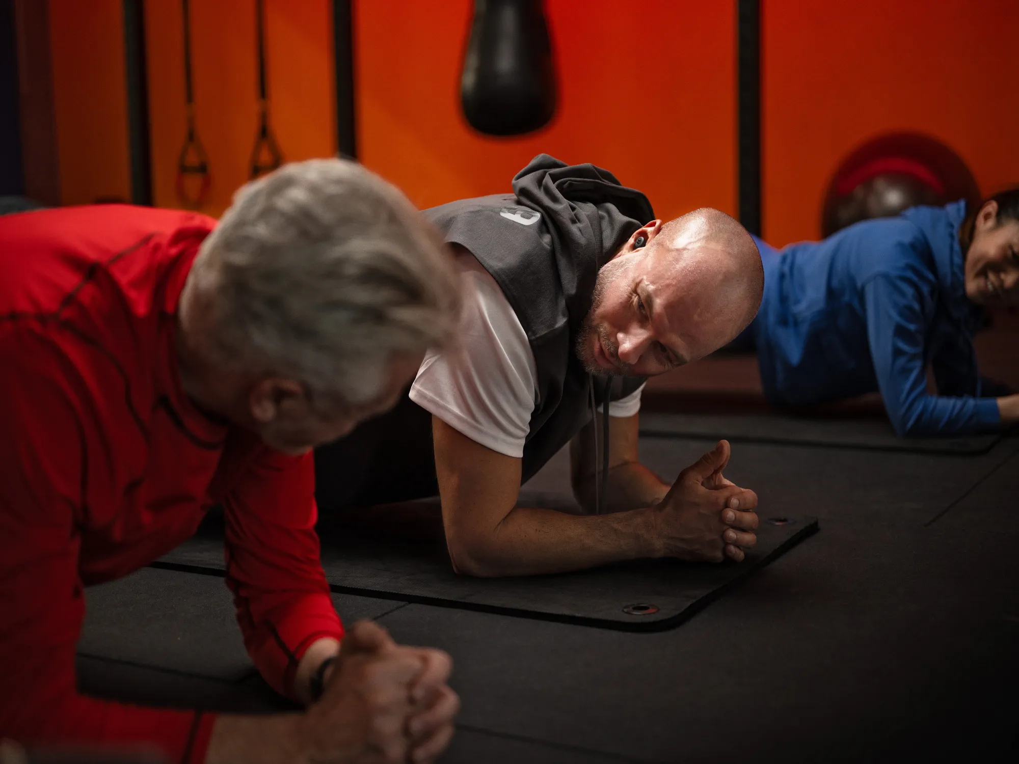 Men and woman with hearing loss using hearing-aids while planking in a gym, staying active and connected during workouts.