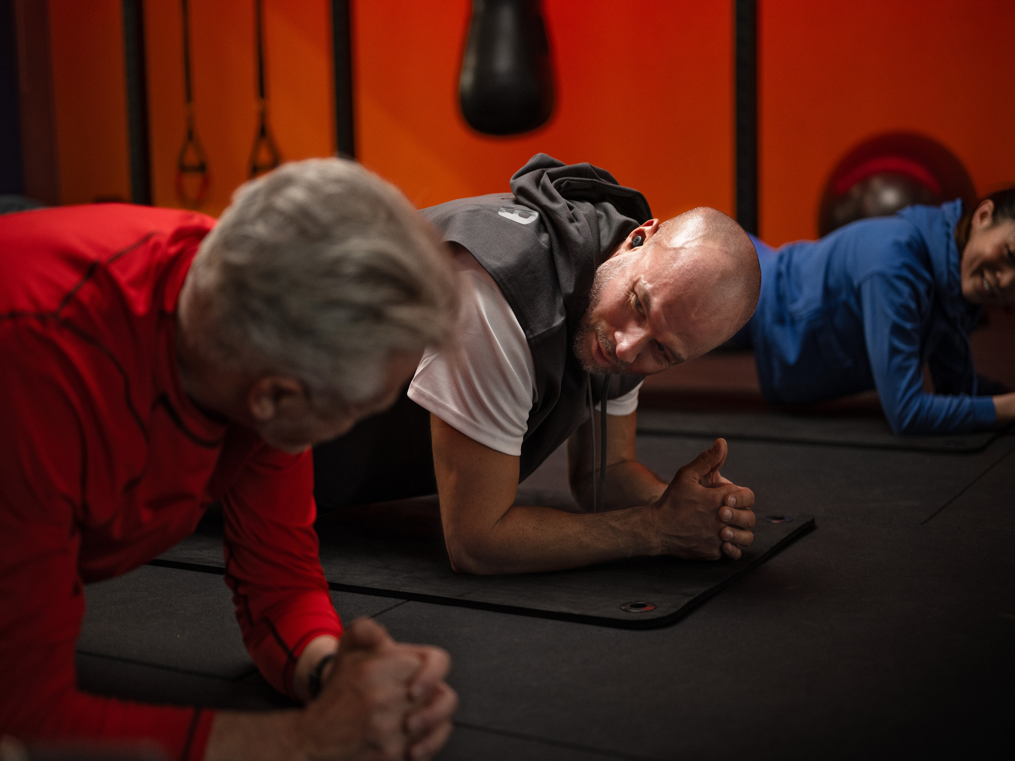 Men and woman with hearing loss using hearing-aids while planking in a gym, staying active and connected during workouts.