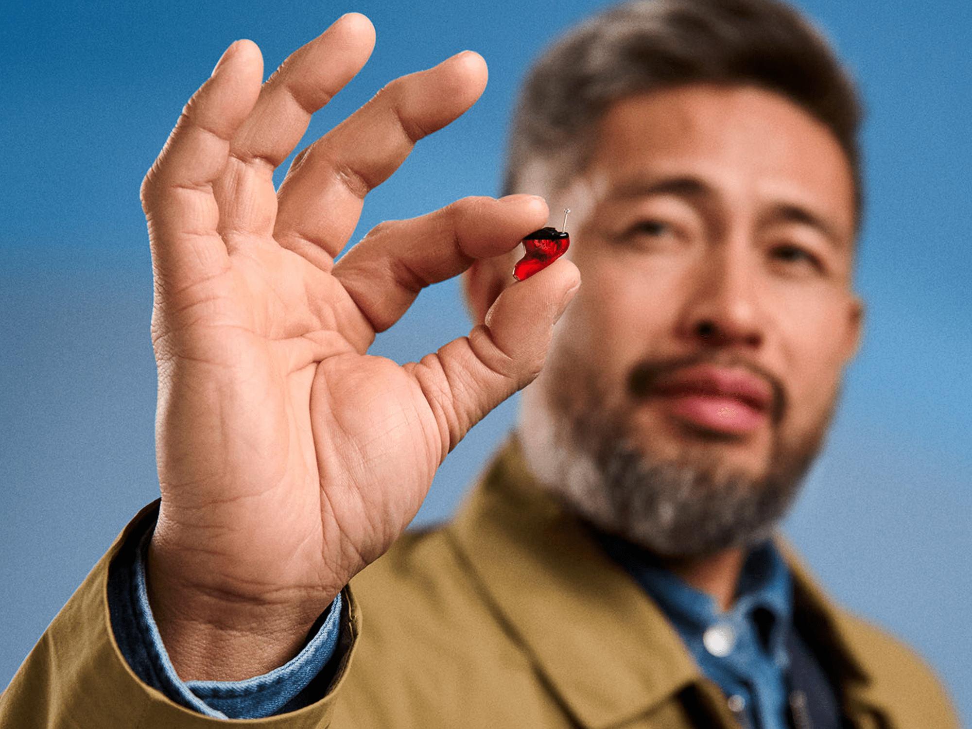 Person with hearing-loss holding a red in-the-ear hearing-aid, showcasing discreet design and easy handling features.