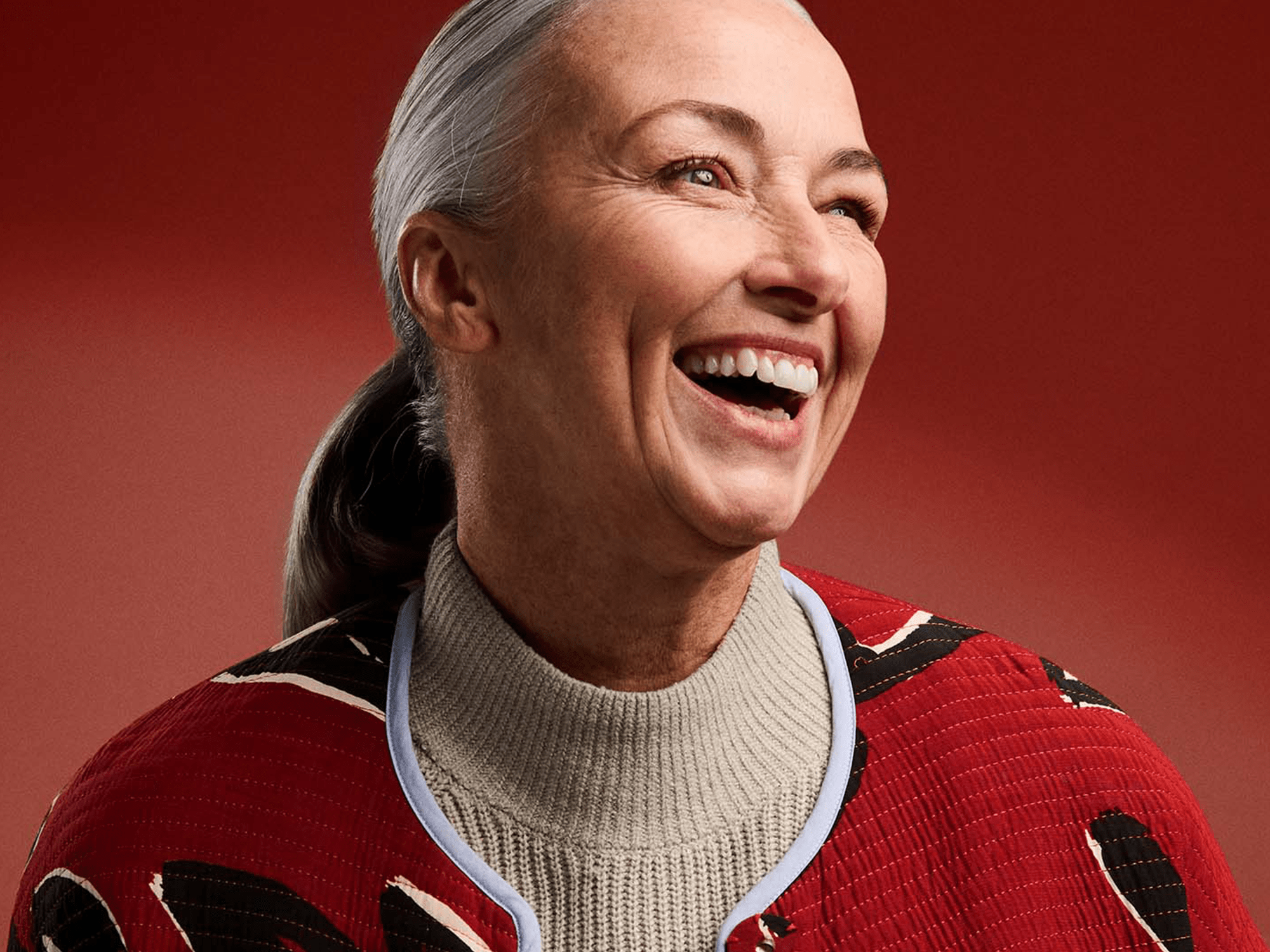 Person with hearing-loss wearing hearing-aids and a red patterned coat, standing confidently against a bold red background.