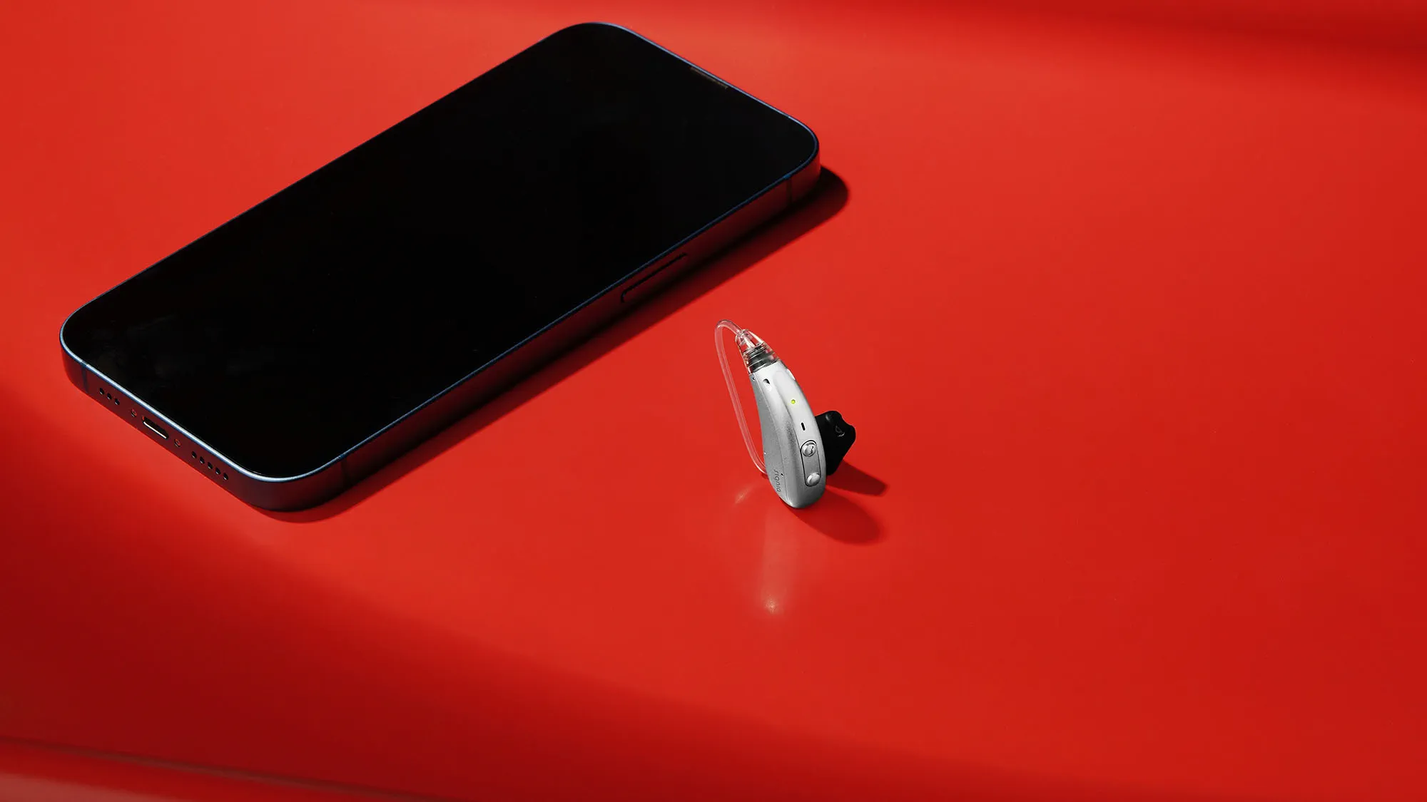 Signia Motion Charge&Go IX hearing aid on table with mobile phone for size comparison.