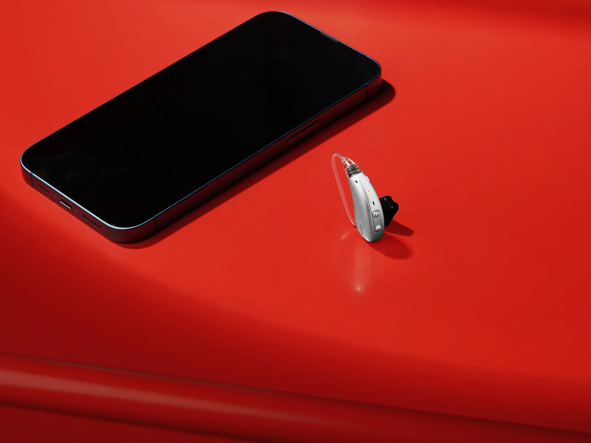Signia Motion Charge&Go IX hearing aid on table with mobile phone for size comparison.