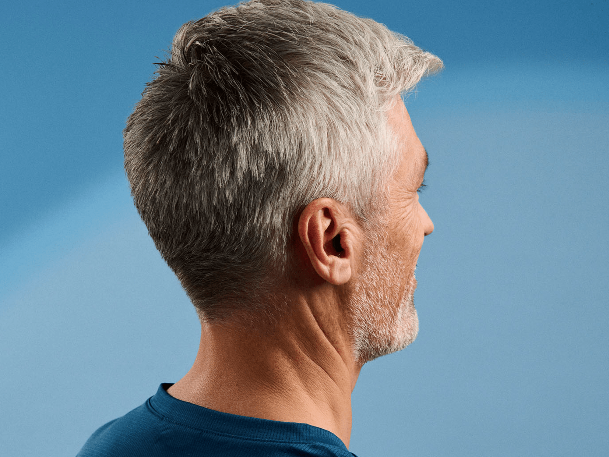 Close-up of the back of a senior person's head with short gray hair, wearing a blue shirt, set against a blue gradient background—highlighting age-related hair texture and color.