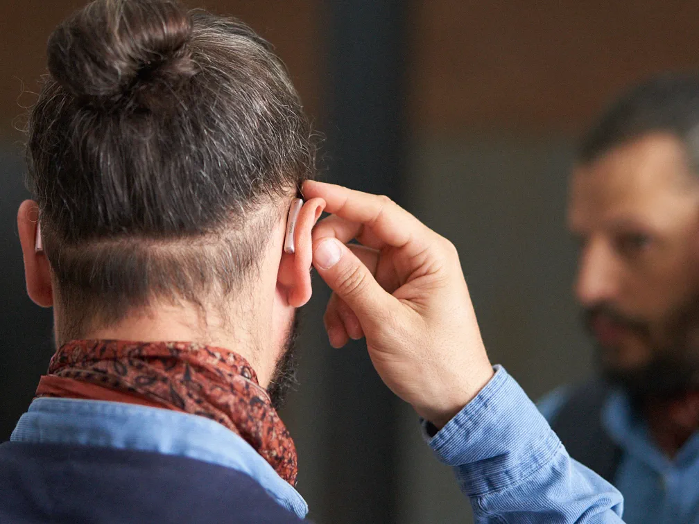 Mann passt sein neues Styletto-Hörgerät an, bevor er sich mit Freunden trifft.