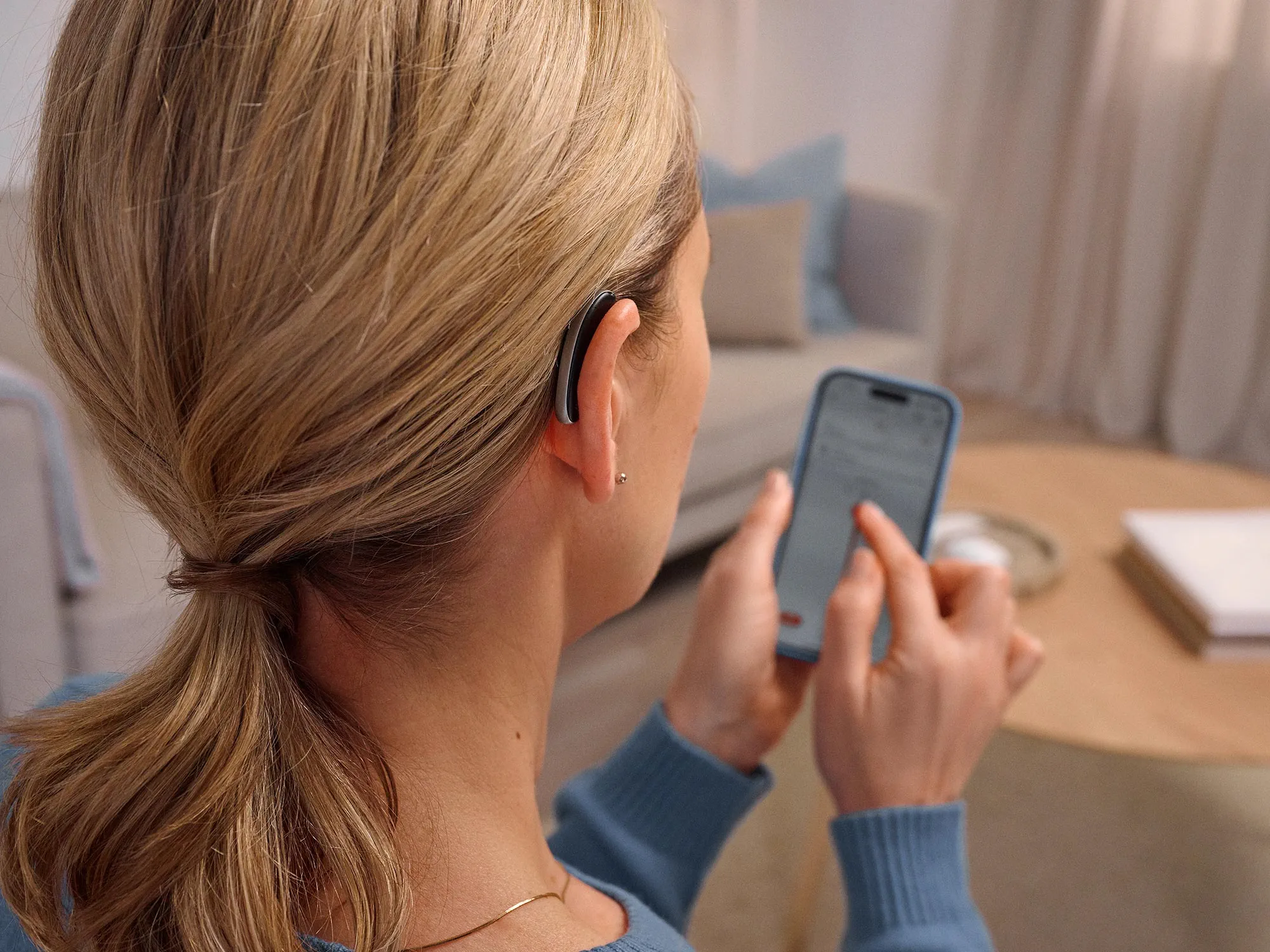 Frau am Telefon, die Signia Styletto Hörgeräte trägt und die Hörgeräte am Telefon steuert