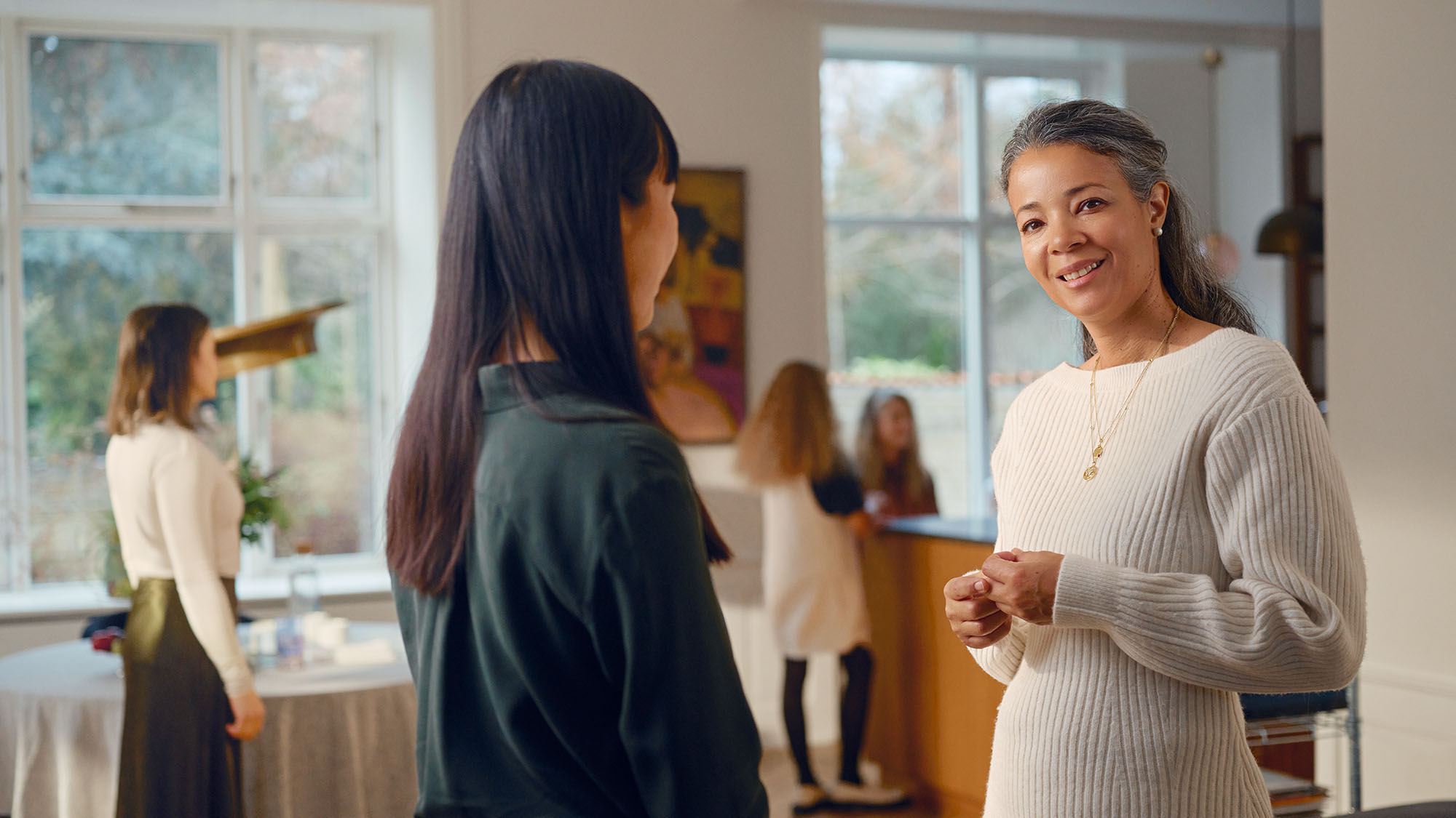 Woman wearing Widex Allure nearly invisible hearing aids at a party while talking to her friend being able to hear it all.