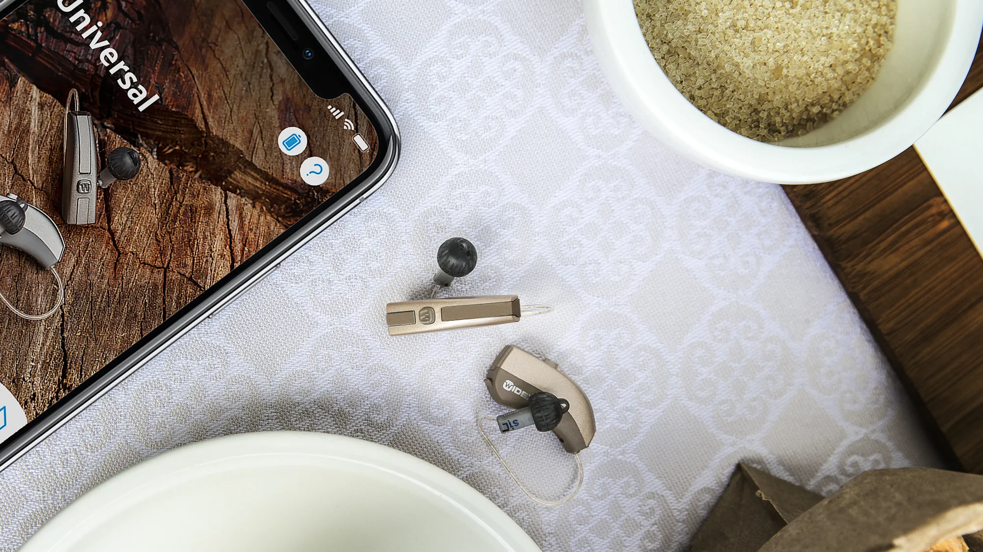 Widex Evoke Hörgeräte auf einem Tisch im Größenvergleich mit einem Smartphone gezeigt.