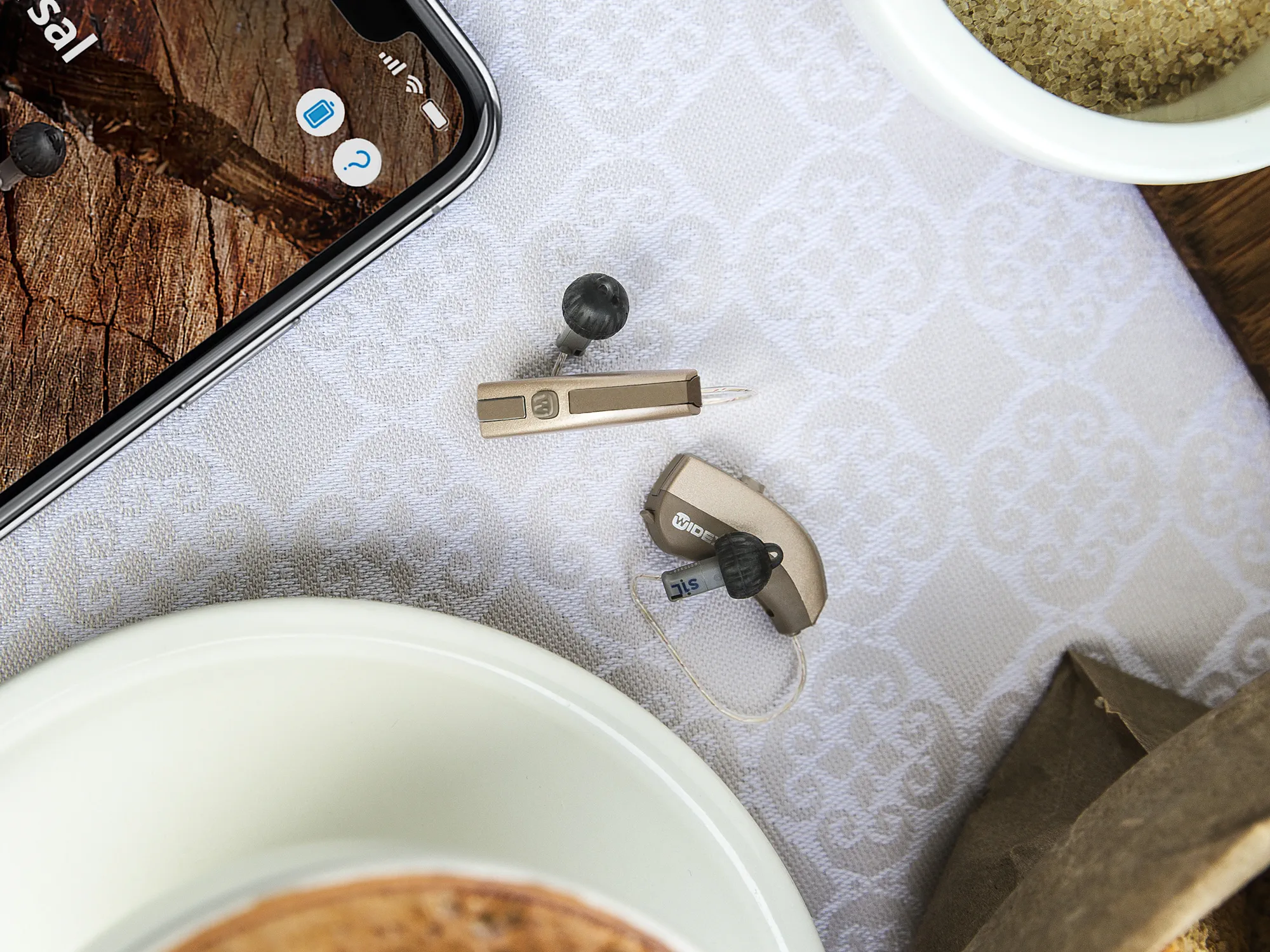 Widex Evoke hearing aids shown on tablle compared to a smart phone in size.