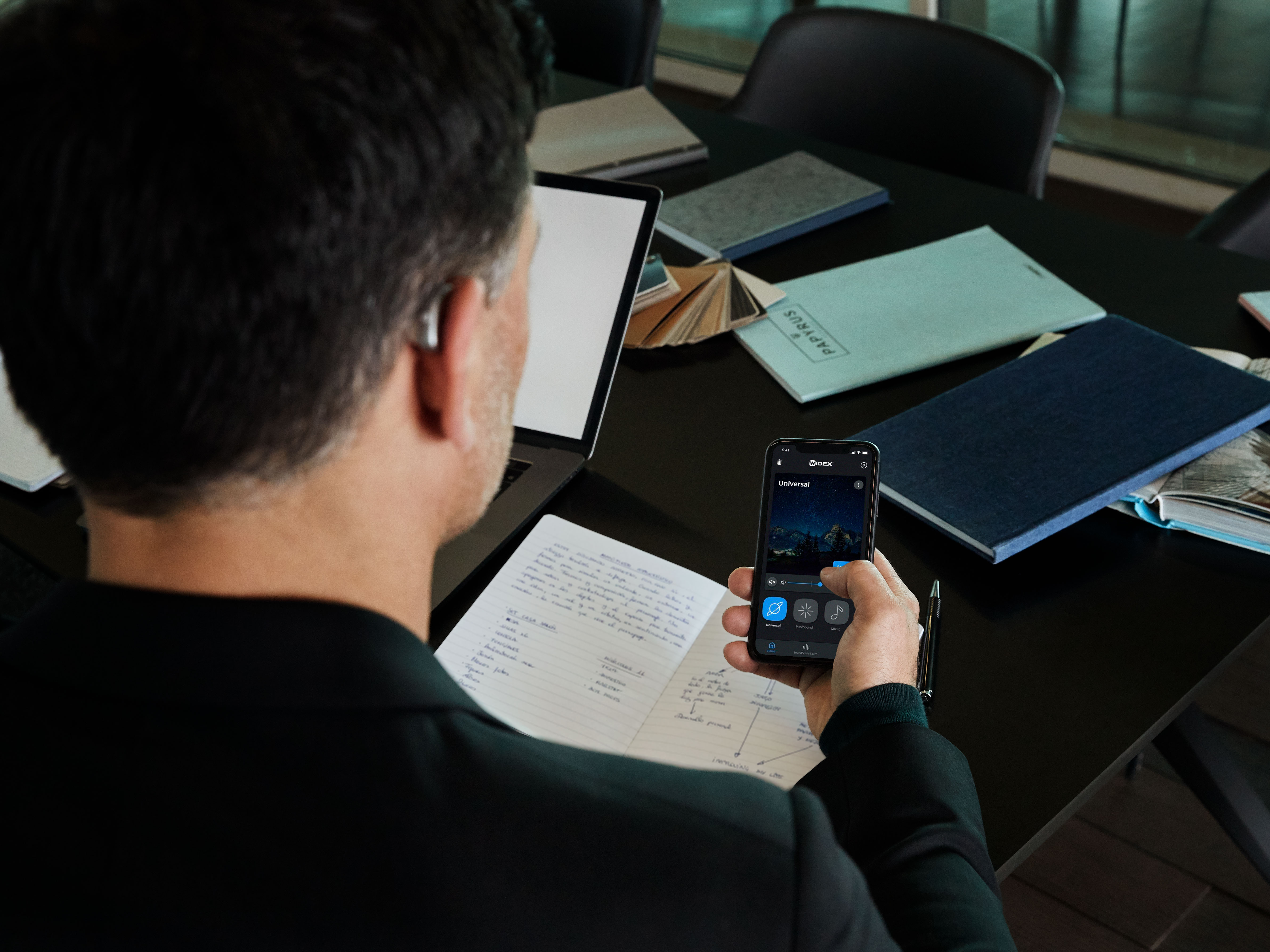 Mann mit Widex Moment Hörgeräten, der seine Hörgeräte mit der Widex Moment Handy-App steuert.