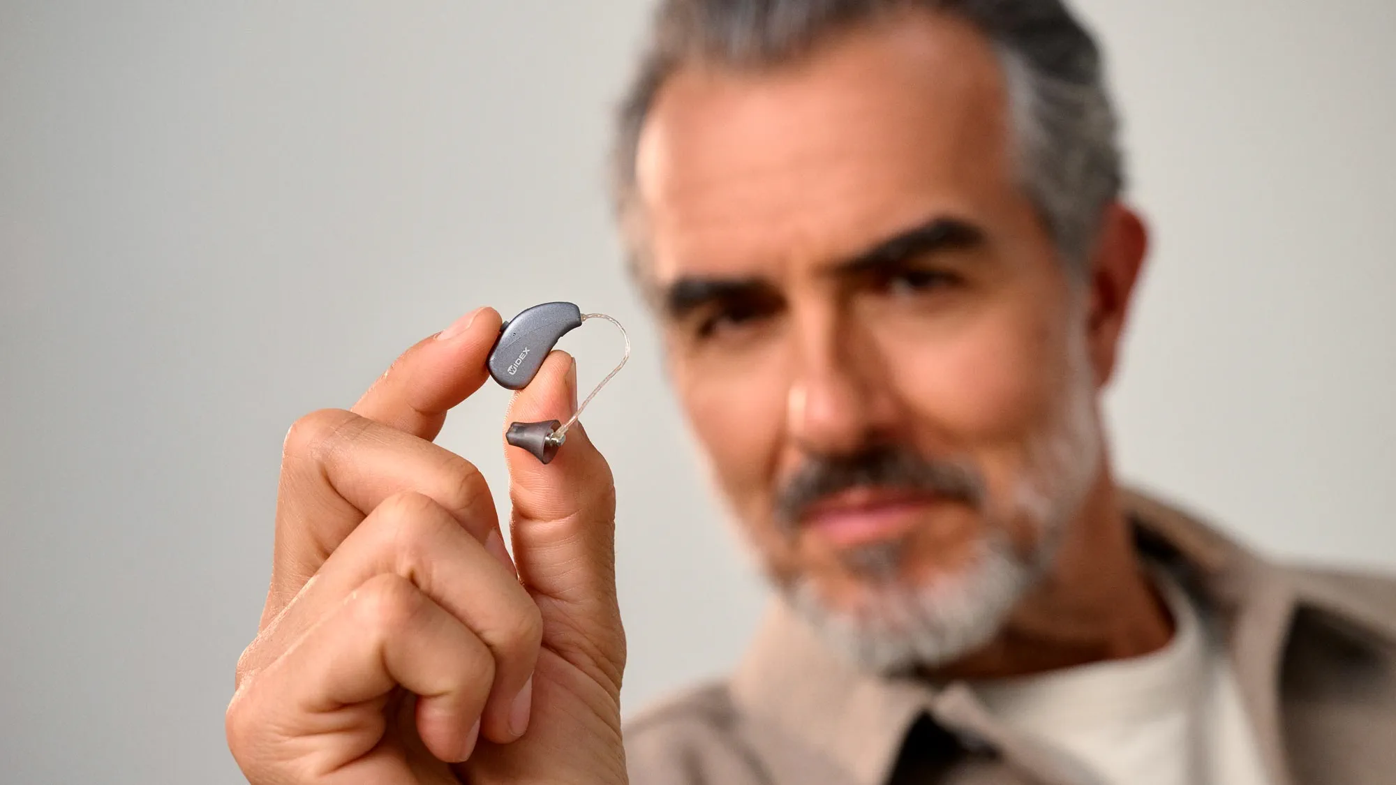 Man holden a the tiny nearly invisible Widex Moment Sheer SRic hearing aid between his finger to show how small they are.