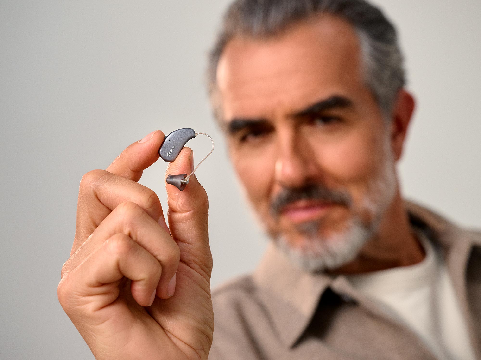 Man holding a the tiny nearly invisible Widex Moment Sheer SRic hearing aid between his finger to show how small they are.