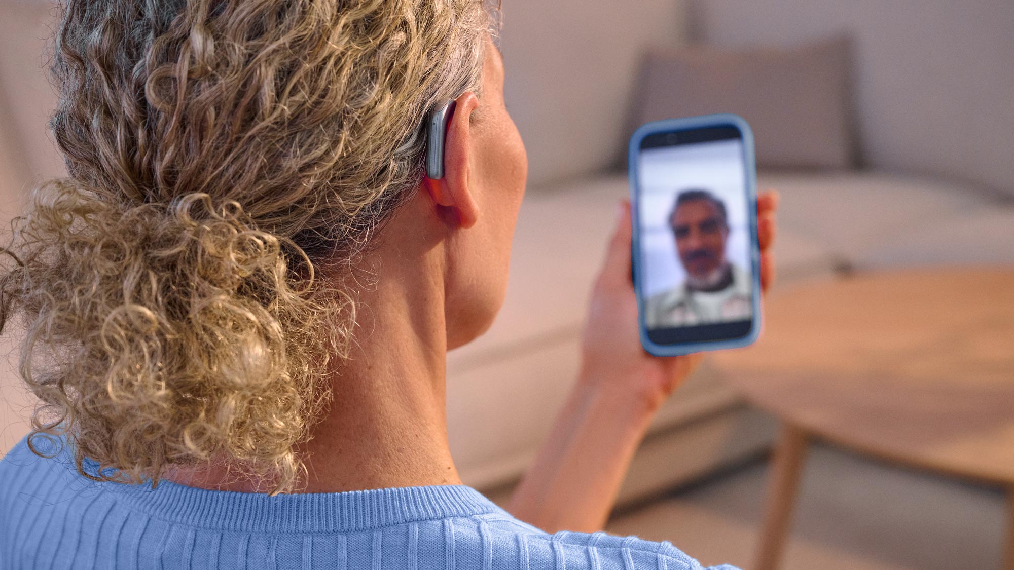 Frau telefoniert per Facetime mit einer Freundin und trägt dabei Widex Smart RIC Hörgeräte, die den Ton direkt vom Telefon an die Hörgeräte übertragen.