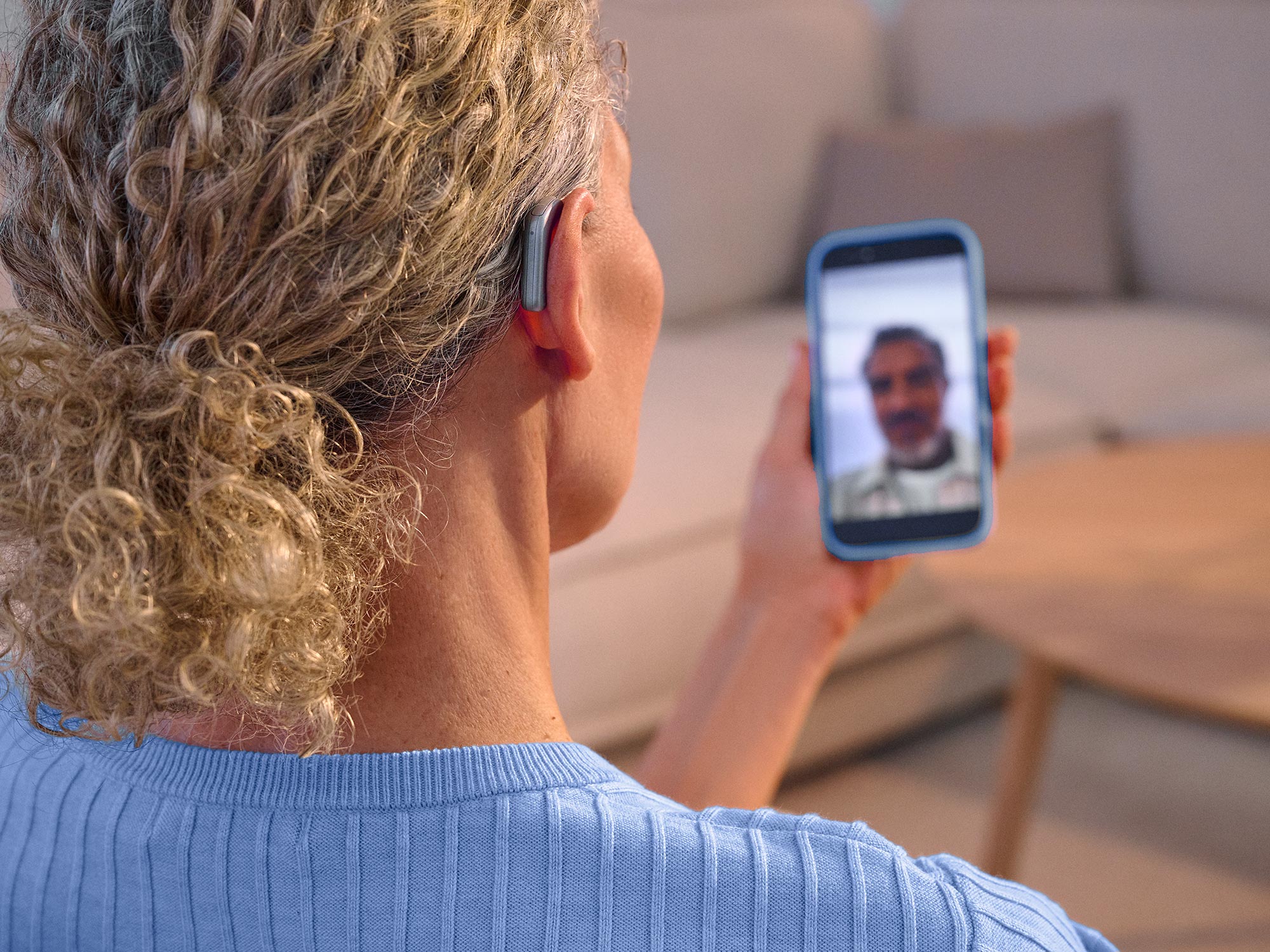 Frau telefoniert und facetimed mit einem Freund und trägt Widex Smart RIC Hörgeräte, die den Ton direkt vom Telefon auf die Hörgeräte übertragen.