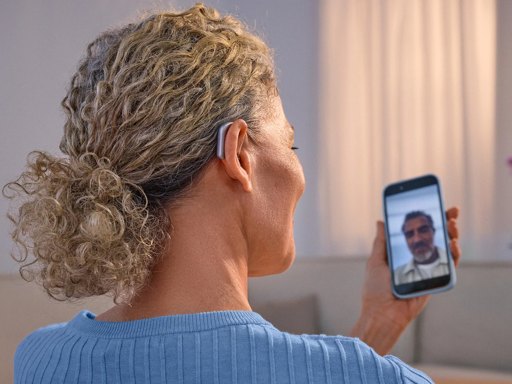 Woman on the phone facetiming with a friend wearing Widex Smart RIC hearing aids getting the sound directly from phone to hearing aids.