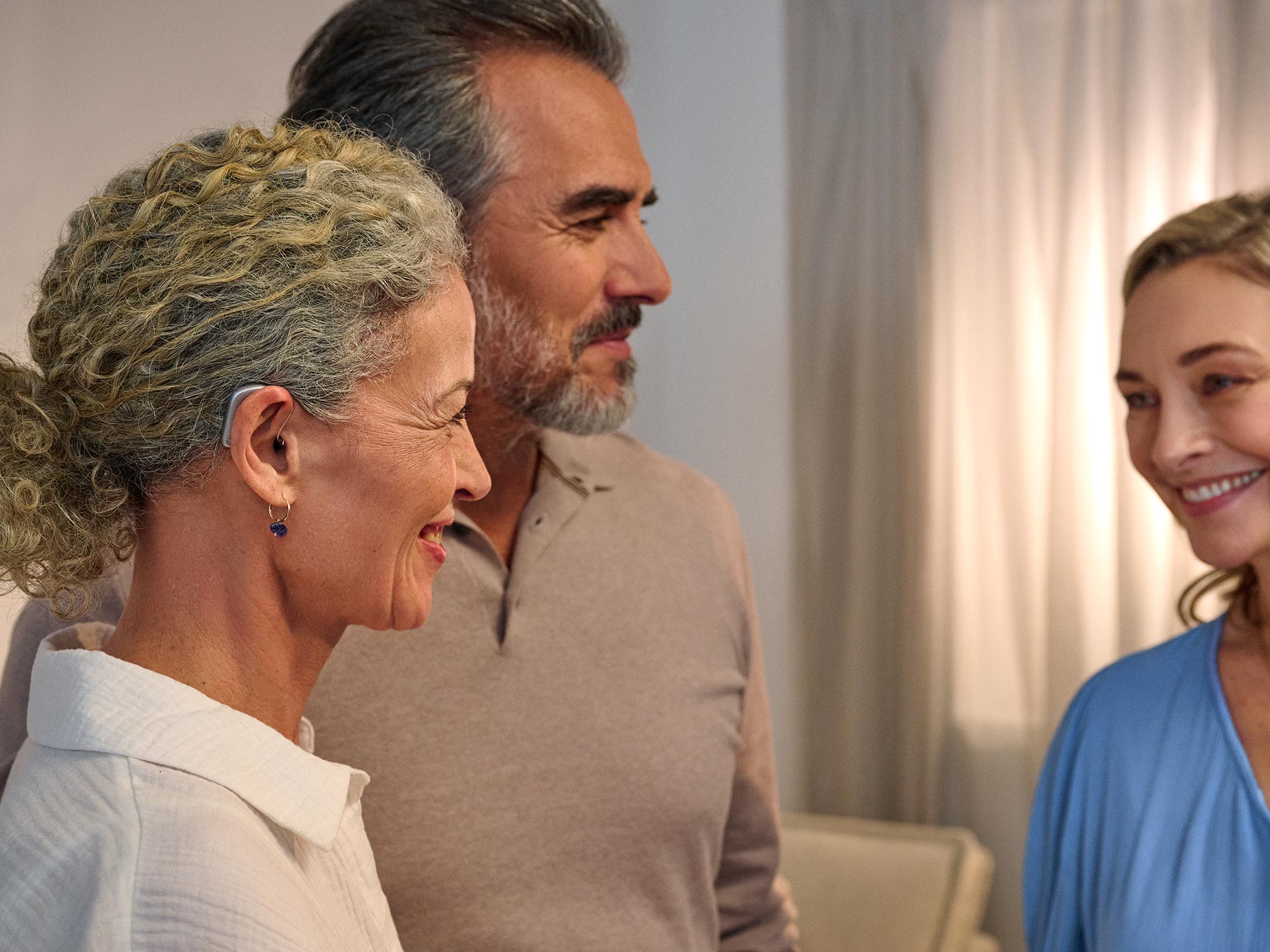 Couple chatting to friend while woman is wearing Widex Smart RIC hearing aids enjoying she can her the converstation