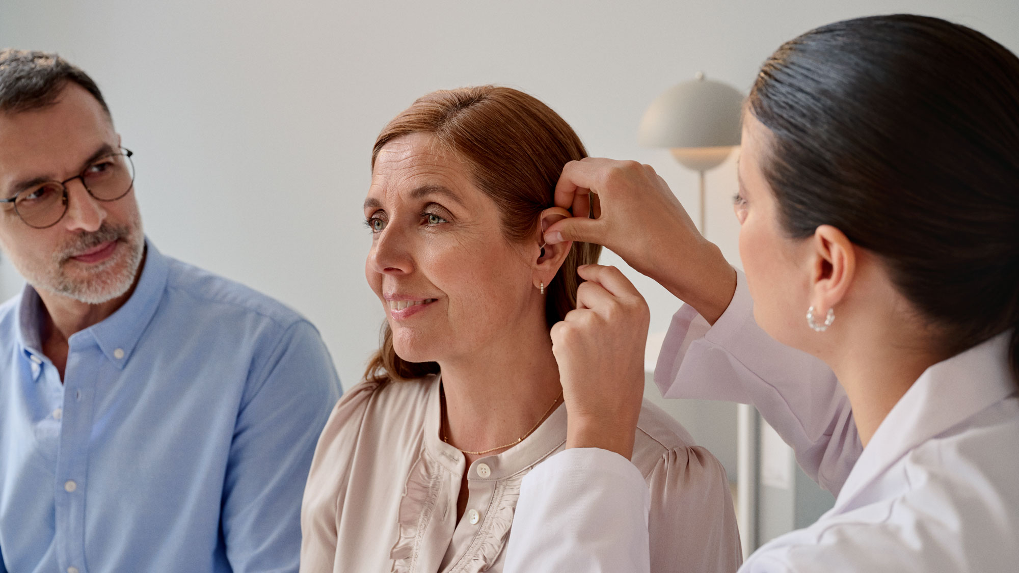 The audiologist fitting a hearing aid onto the customers ear during the hearing appointment.