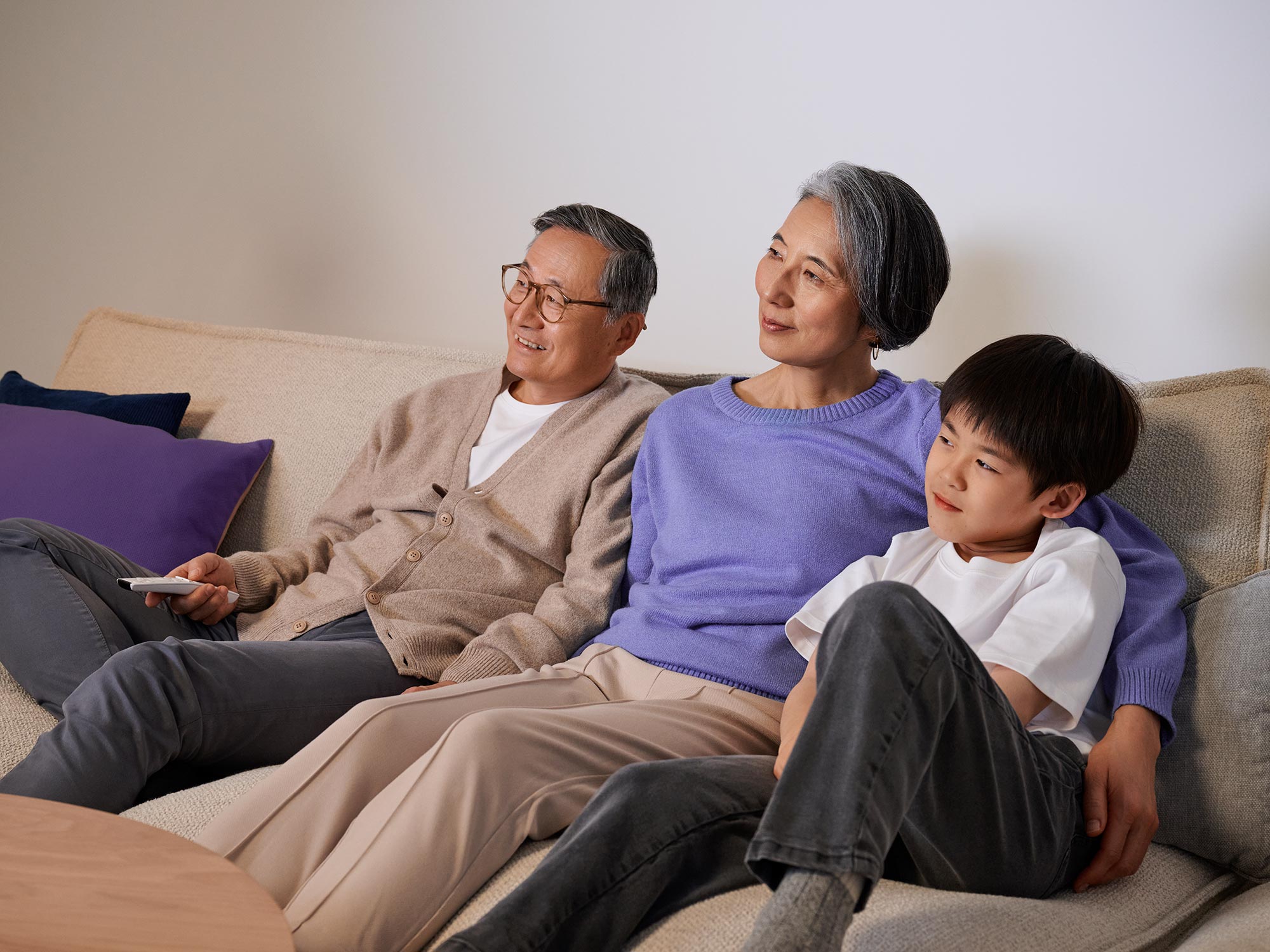 Grandparents comfortably watching TV, shown with hearing aids.