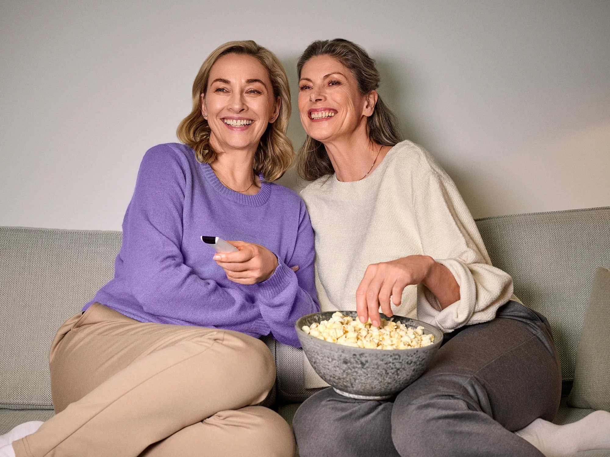 Women laughing together while watching TV, all wearing hearing aids.