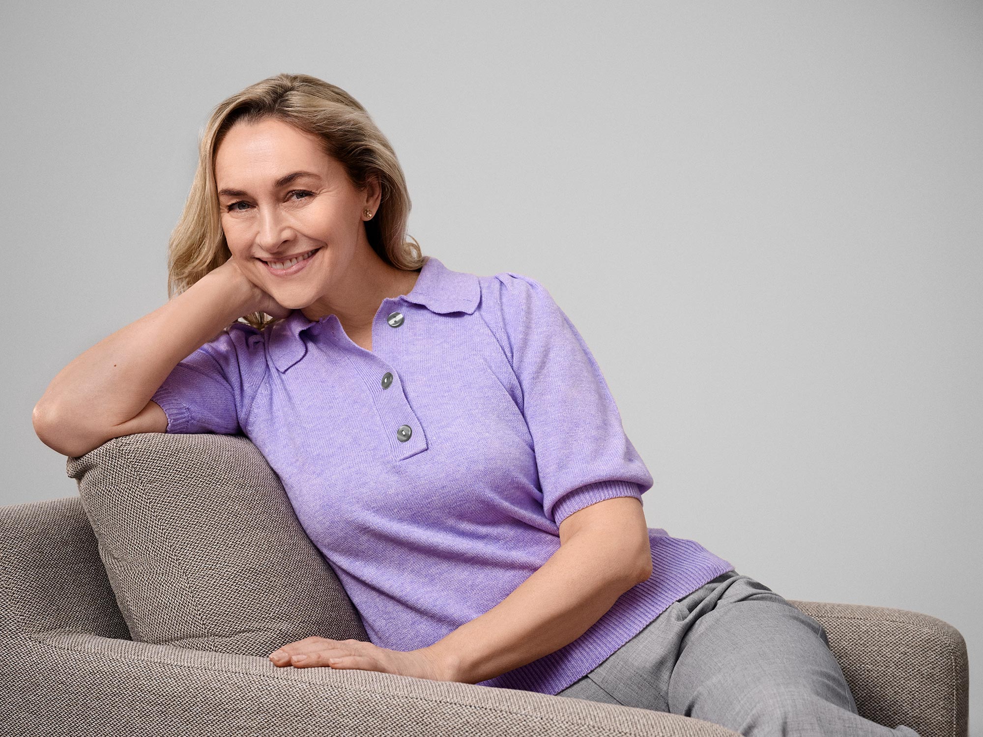 Smiling woman sitting comfortably, wearing hearing aids.