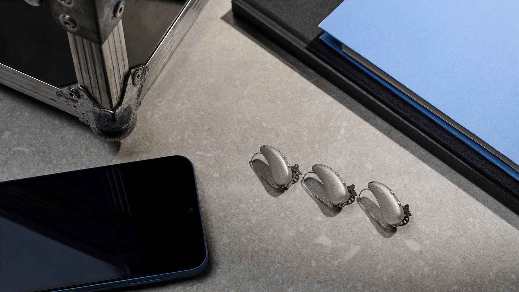 Three Oticon hearing-aids displayed on a desk, offering sleek solutions for individuals with hearing-loss and modern lifestyles.
