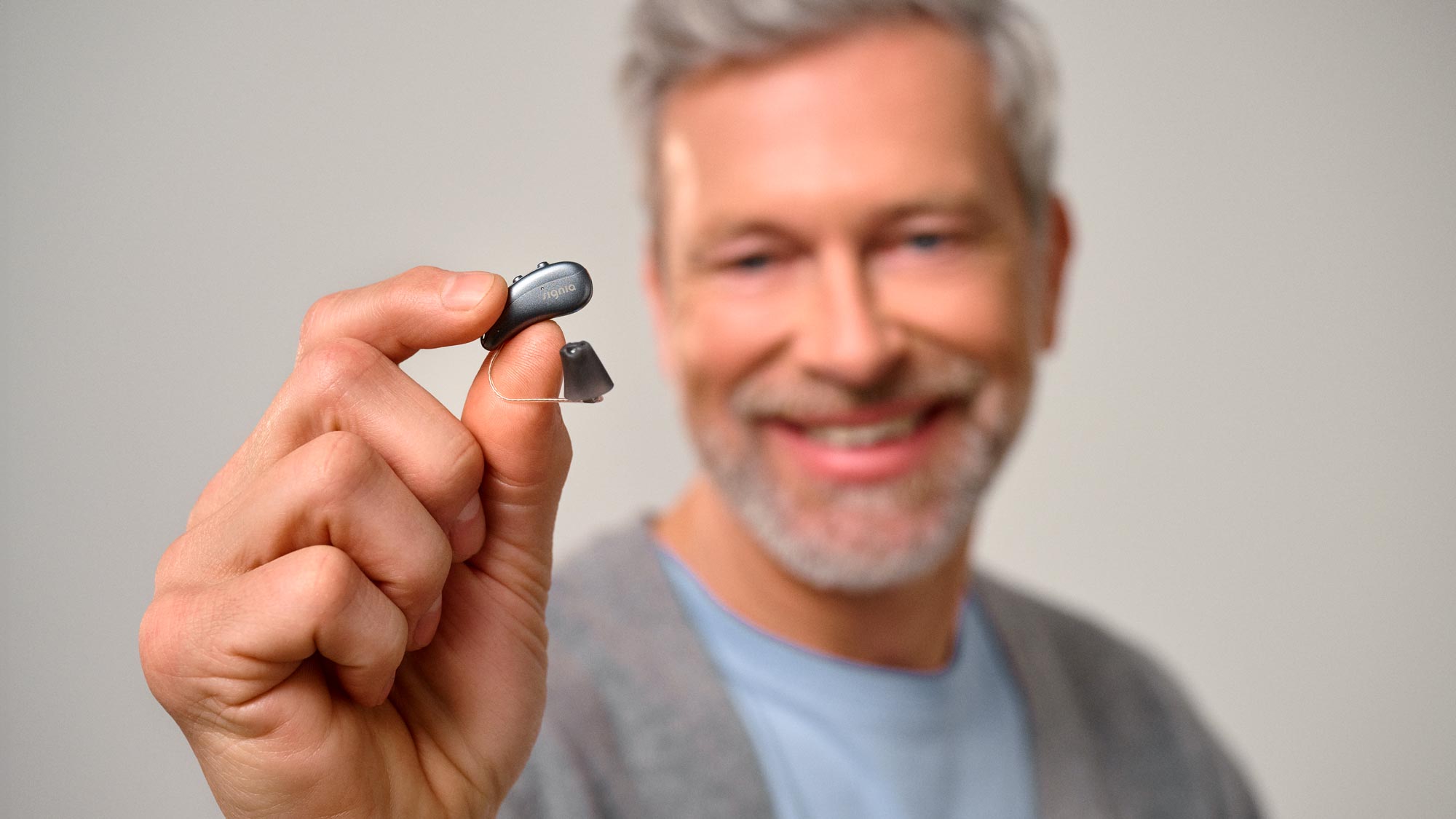 Man holding Signia hearing aid between his fingers to show how tiny it is