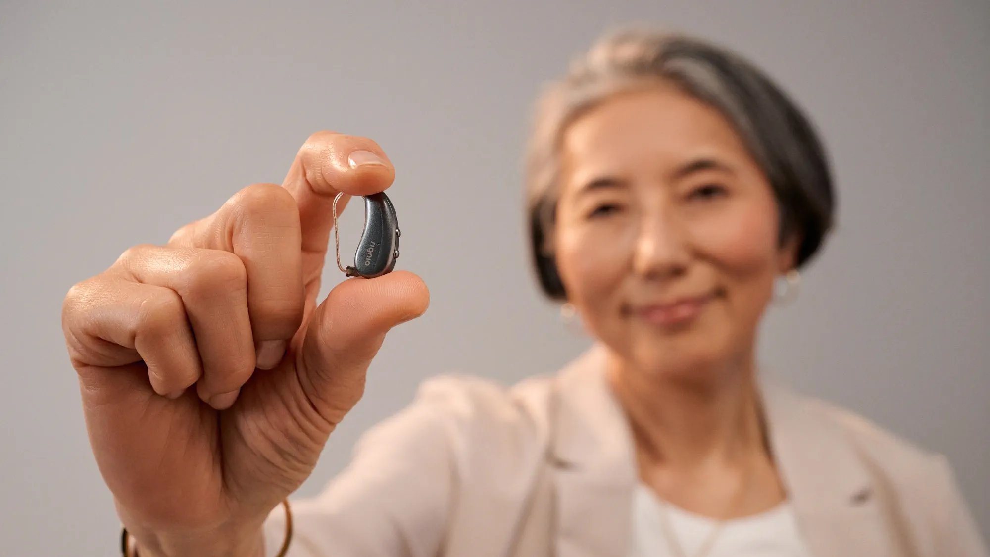 Signia Pure がいかに小さいかを示すために指の間に挟んでいる女性