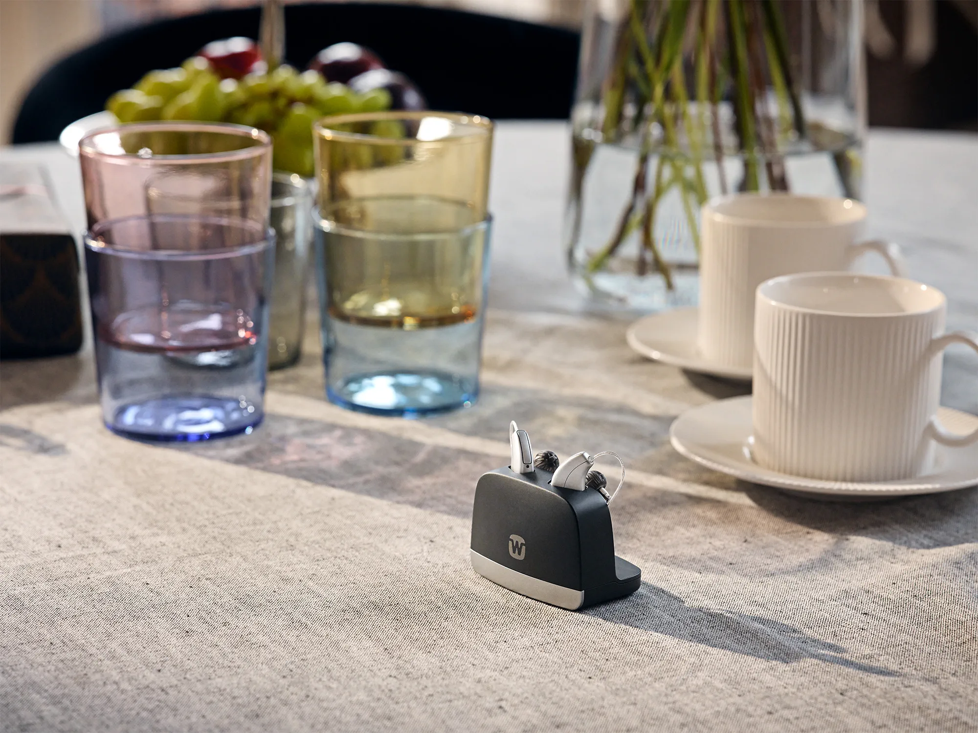 Widex Allure hearing aids shown in charger next to cups to illustrate how small they are.