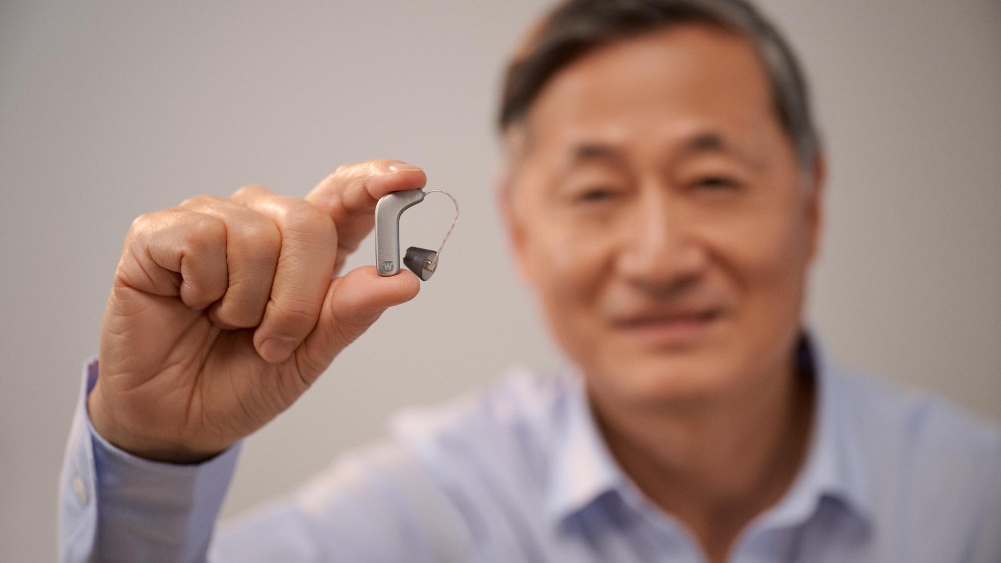 ワイデックス スマート RIC 補聴器を指の間に挟んで、その小ささを見せている男性。