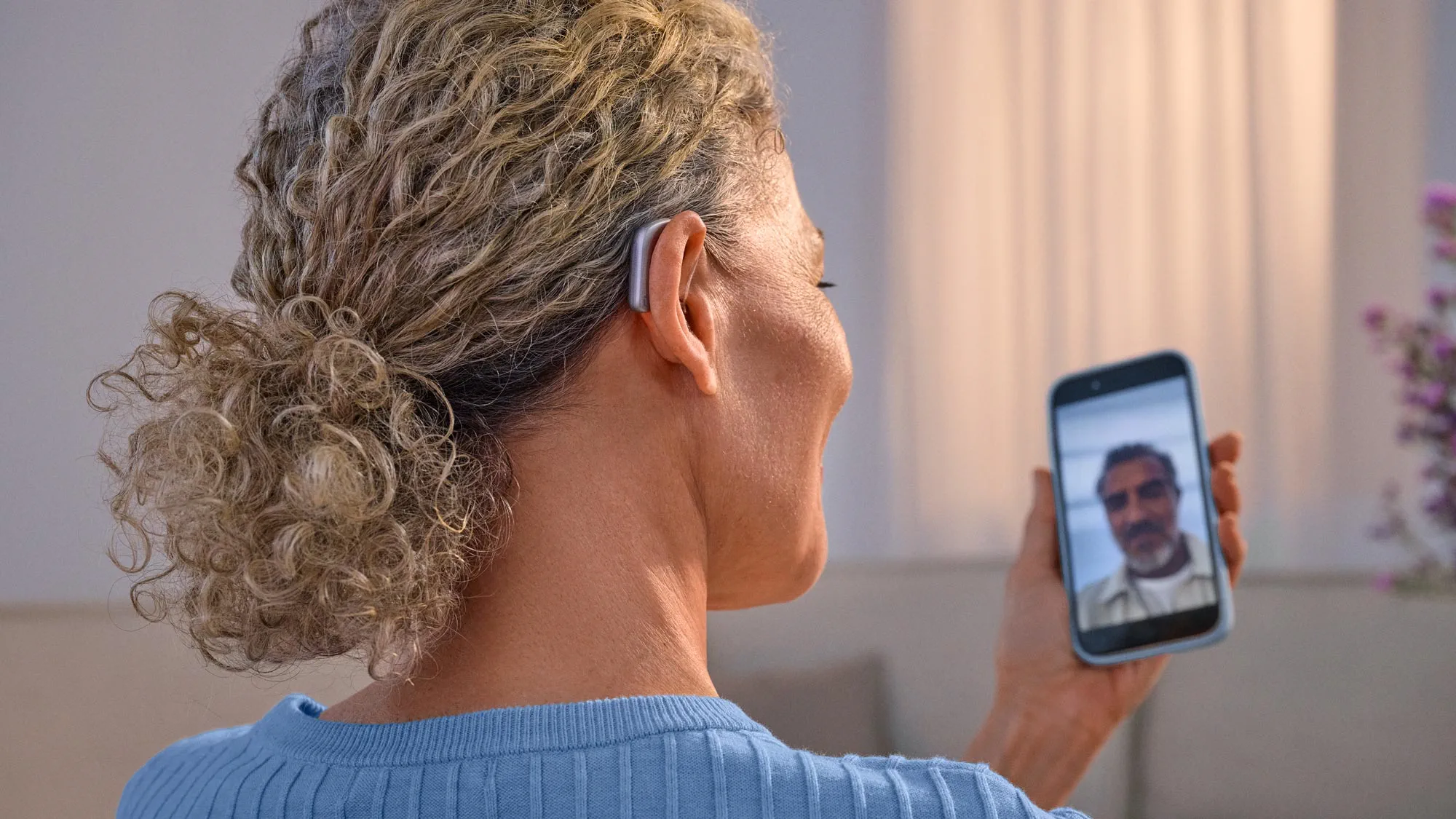 Mulher a fazer uma chamada por videochamada com uma amiga, usando aparelhos auditivos Widex Smart RIC e recebendo o som diretamente no aparelho auditivo.