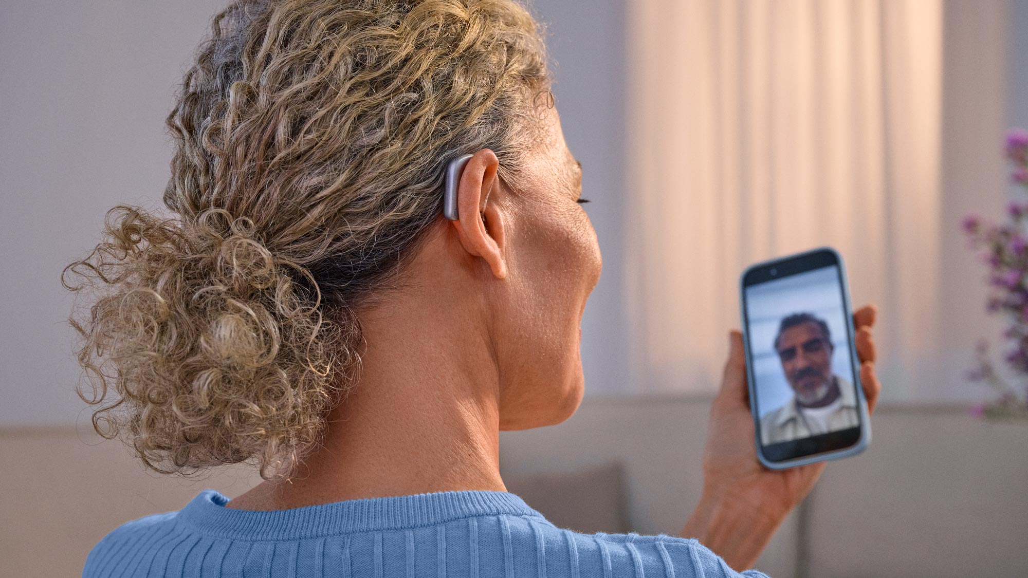 Mulher a fazer uma chamada por videochamada com uma amiga, usando aparelhos auditivos Widex Smart RIC e recebendo o som diretamente no aparelho auditivo.